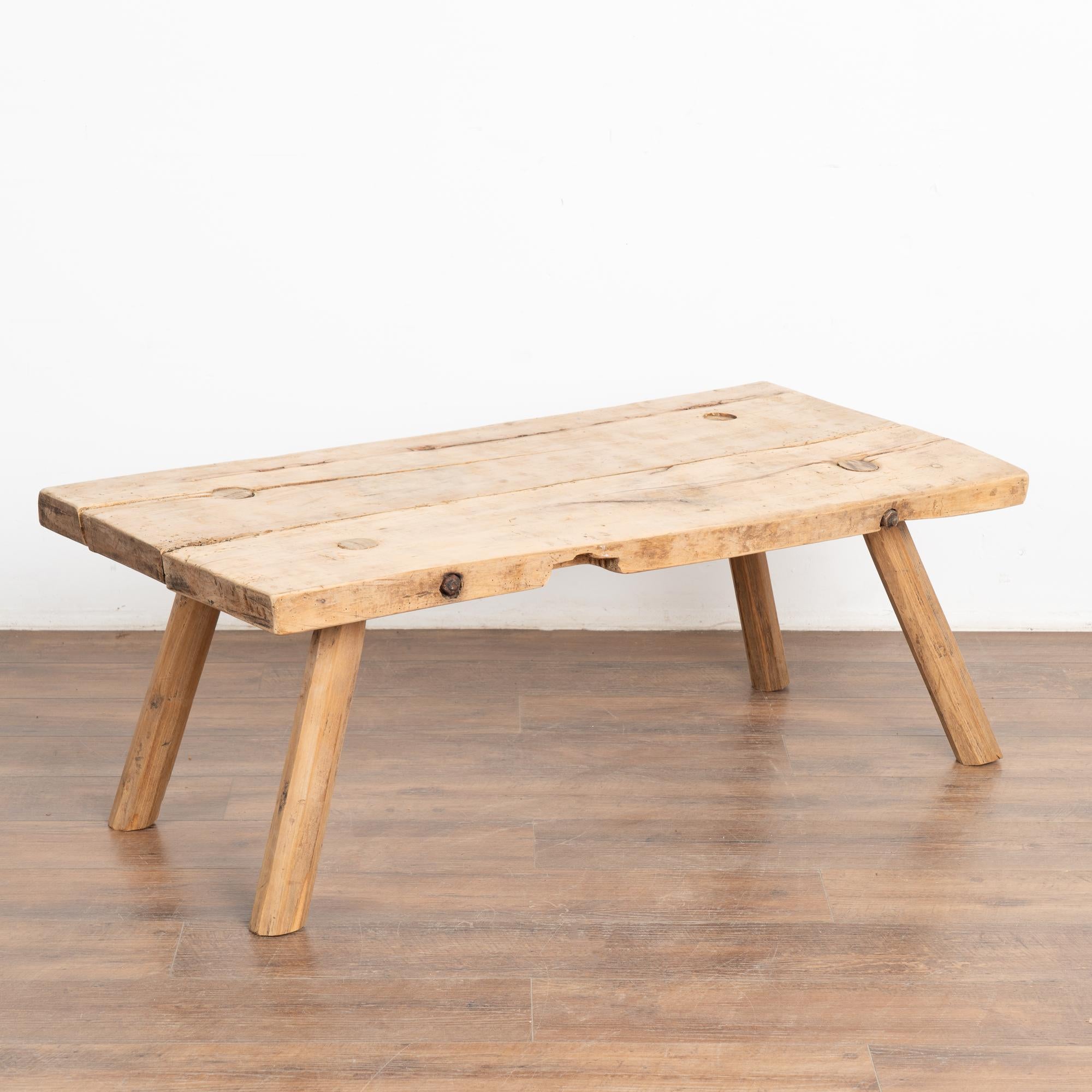 The appeal of this rustic coffee table comes from the thick wood of the top that originally served as a work table. 
Note the gouges, nicks, deep cracks and old dried worm holes that all combine to build the vintage character of this coffee table.