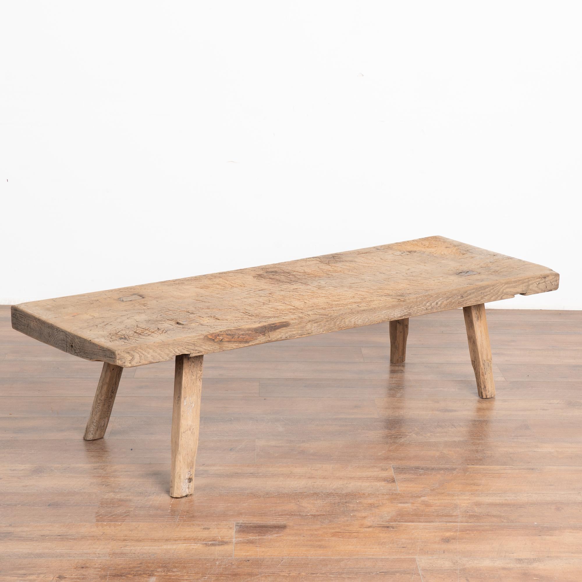 The appeal of this rustic coffee table comes from the thick wood of the top that originally served as a work table.
The slab of wood that serves as the top is impressive and creates the desire to touch it. Note the heavy wear including gouges,