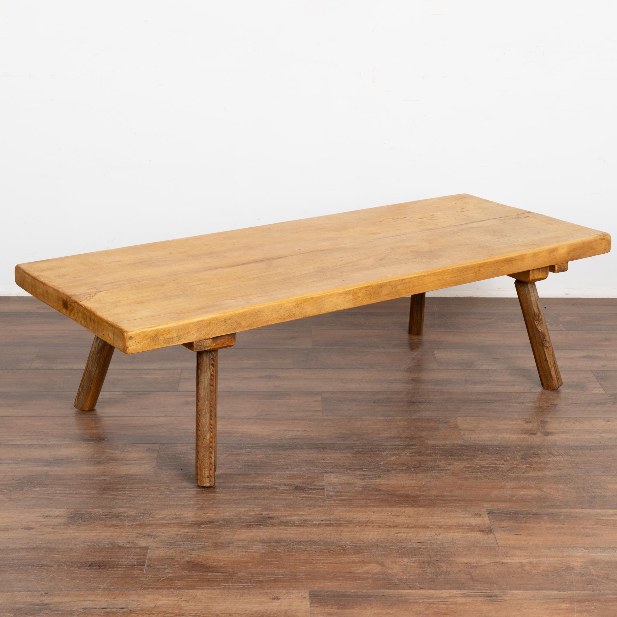 The appeal of this rustic coffee table comes from the thick wood top that originally served as a work table. 
The round peg legs are a contrasting darker color that the top.
Note the scratches, nicks, and even cracks that all combine to build the