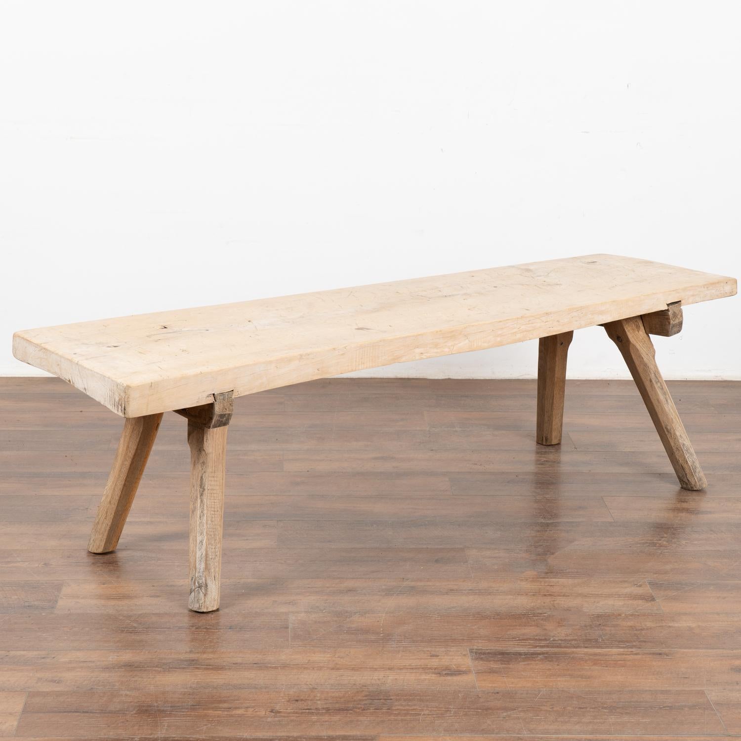 The appeal of this coffee table comes from the rustic wood top that originally served as a work table and rests on original thick peg legs. 
The many scratches, nicks, deep gouges, stains and old cracks that all combine to build the depth of