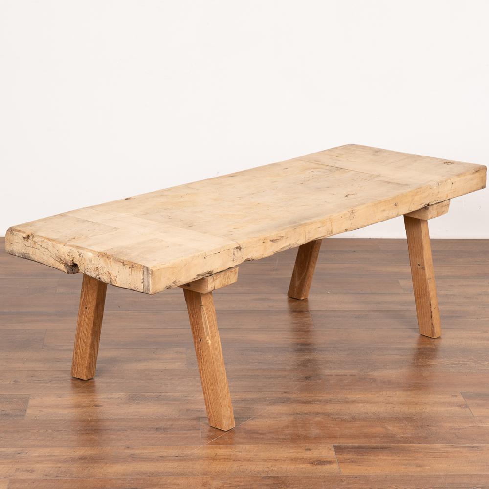 The appeal of this rustic coffee table comes from the thick wood of the top that originally served as a work table. 
Note the gouges, nicks, old cracks and inlaid wood pattern that all combine to build the vintage character of this coffee table.