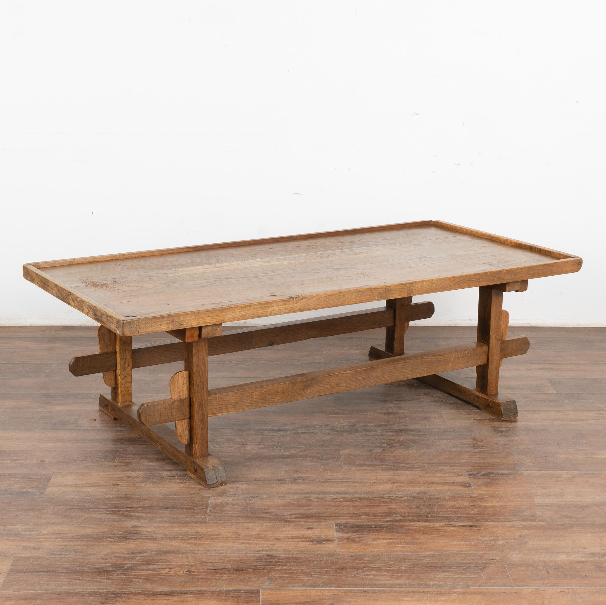Rustic 5.5' farmhouse coffee table with trestle style base and rim around table top; loaded with vintage character.
The warm patina of the oak top reveals scrapes, gouges, stains and old cracks acquired with 100 years of use as a work