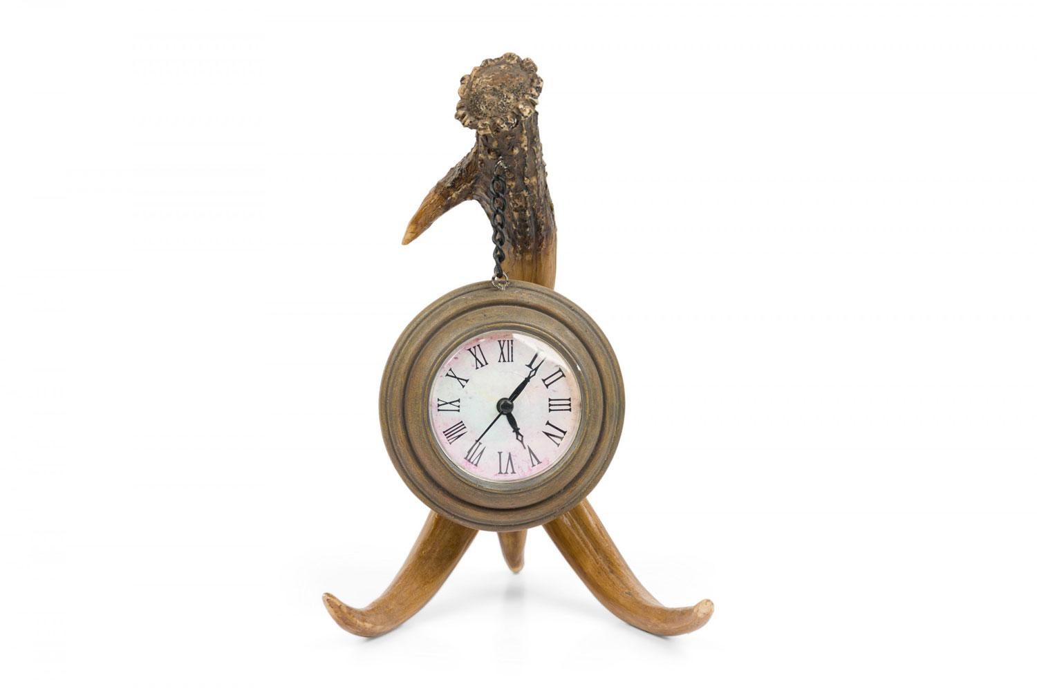 Rustic Continenetal-style table clock with a resin faux antler stand suspending a brass cased black and beige enamel-faced clock from a small chain.