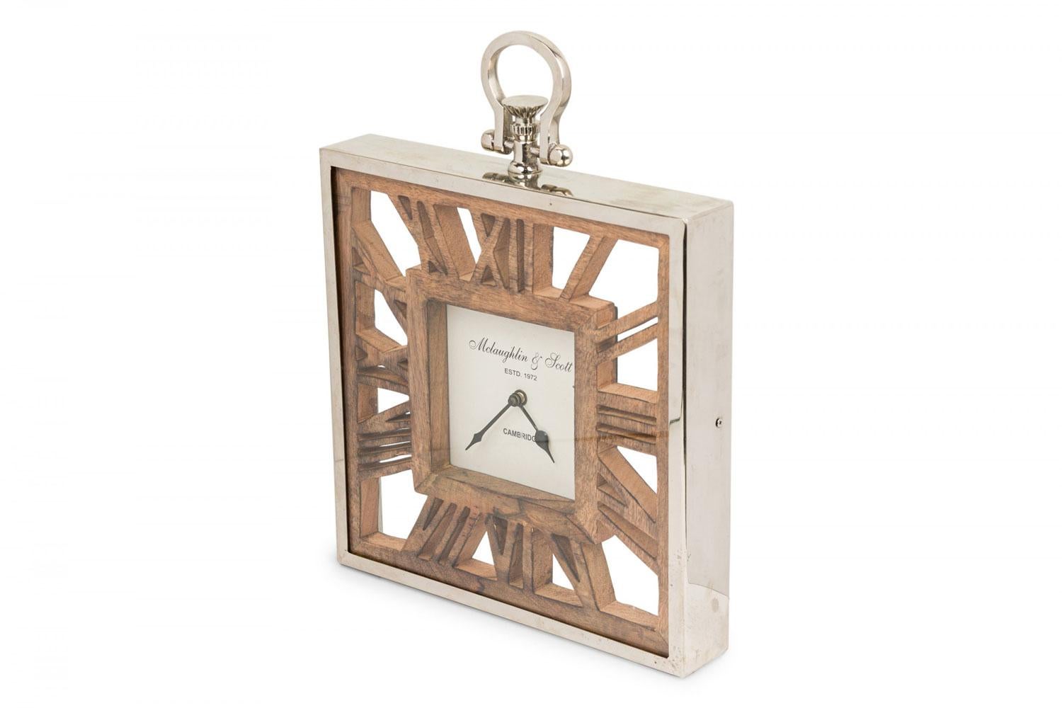 Rustic Continental-style square table or wall clock with a silver metal and glass case containing carved wooden Roman numerals surrounding a central beige and black clock face, topped with a metal eyelet for hanging (Mclaughlin & Scott).