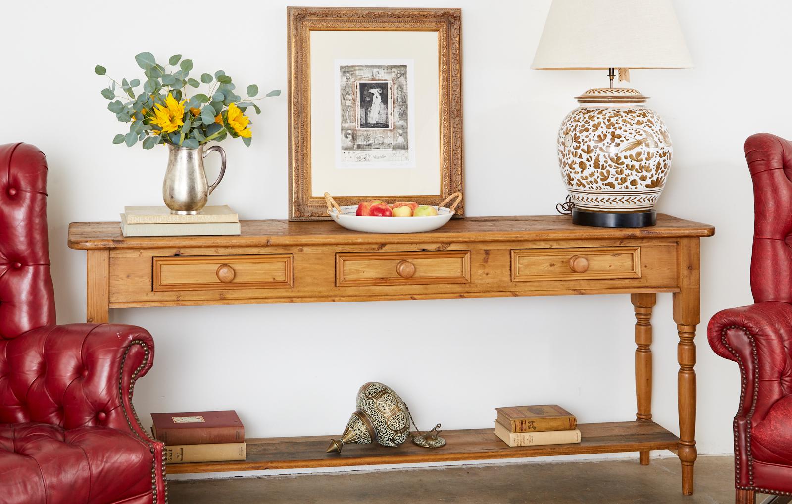 20th century rustic country American pine three-drawer console table or sofa table. Features a two-tier design with a large lower display shelf. The case is fitted with three drawers having wood knob pulls. The shelf and thick top have a beautifully