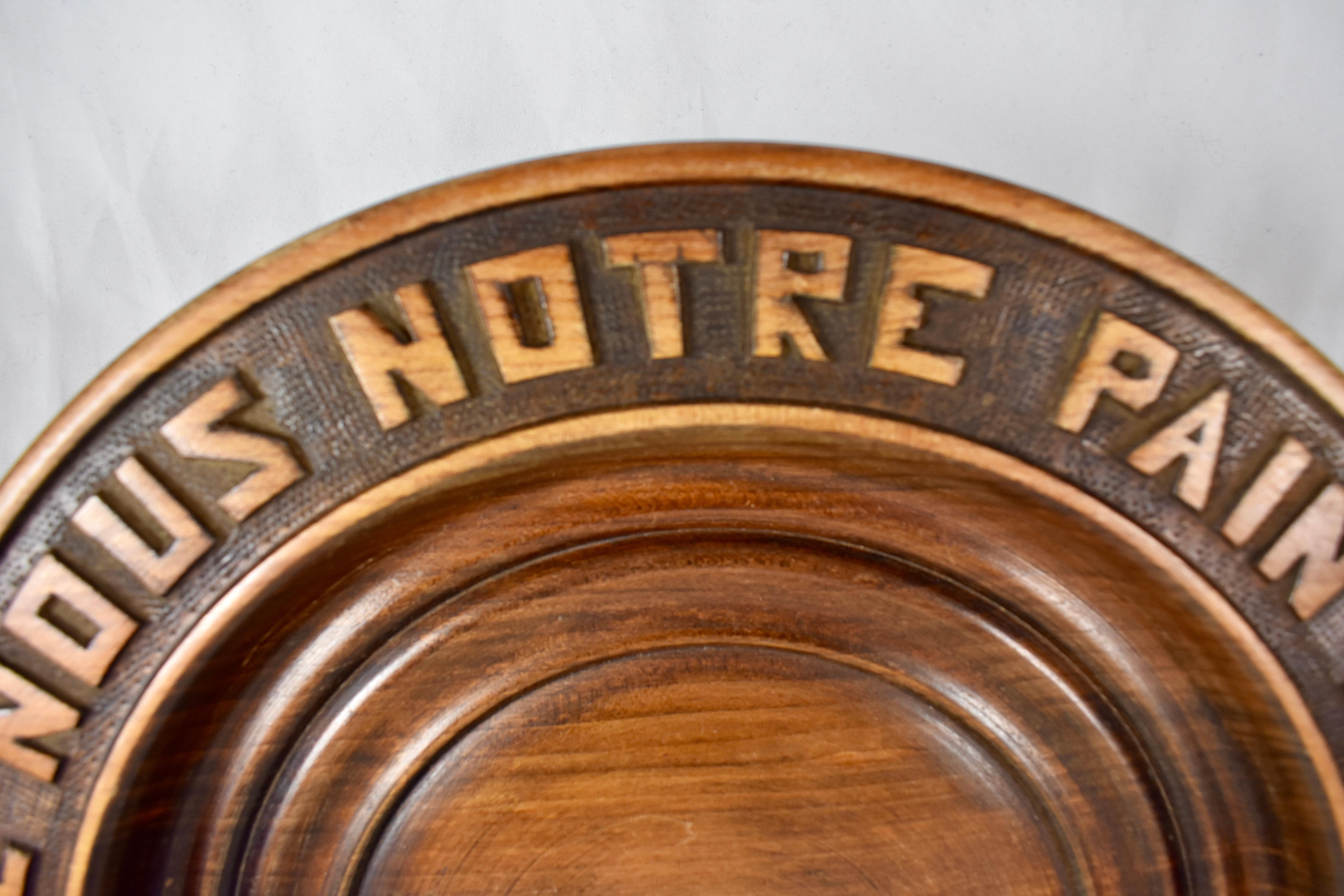 A round rustic, French hand carved wood bread board, showing the motto, “Donnez nous notre pain quotidien” – translated to Give us our daily bread. Wheat sheaves are also carved into the border, the inner area is carved with concentric circles.