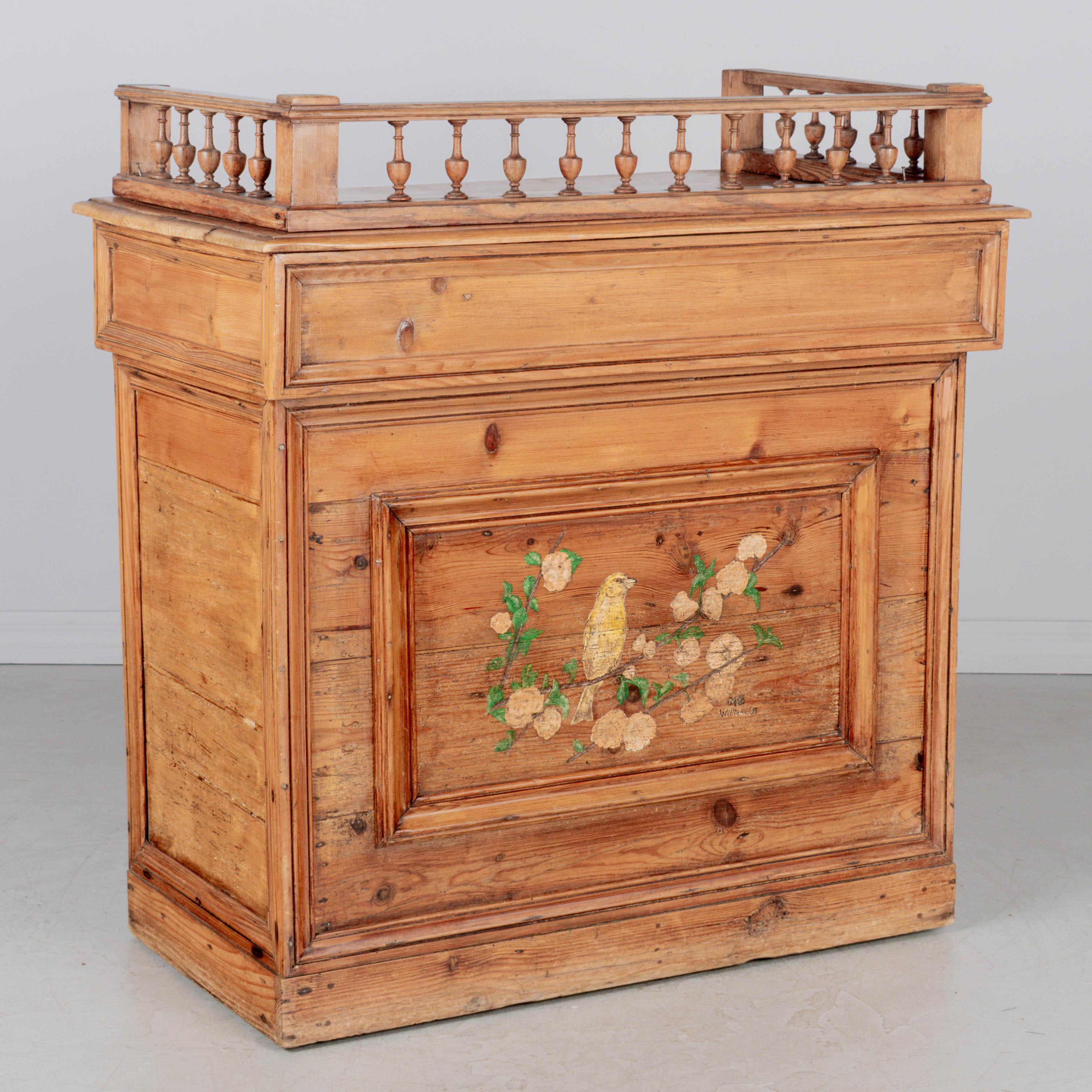 A rustic Country French comptoir or store counter, made of pitch pine with trimmed panels and decorated on the front with a hand-painted yellow bird on a blossoming tree branch. Painting likely added at a later date signed: MB William '33. The top