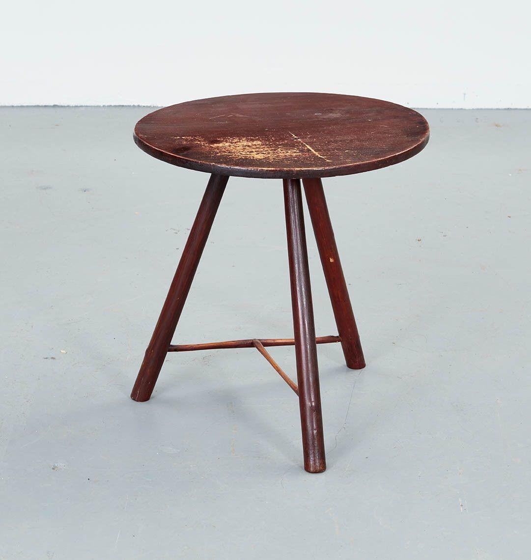 An early 19th century rustic vernacular cricket table with red wash having a round top with three spoke shaved pole legs fixed to a hewn underside block and joined by a 