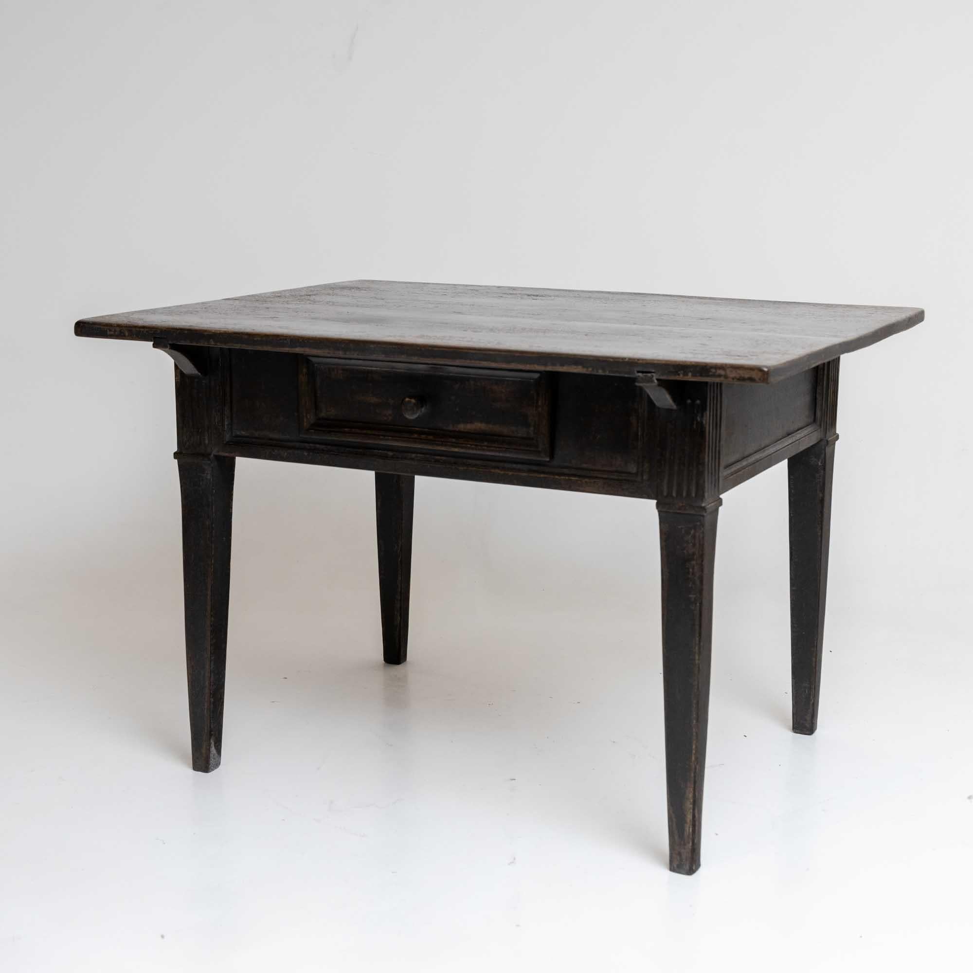 Rustic dining table with one drawer and rectangular table top. The table stands on tapered legs with fluted decorations on the frame. The dark gray dining table has been repainted and given an antique patina.