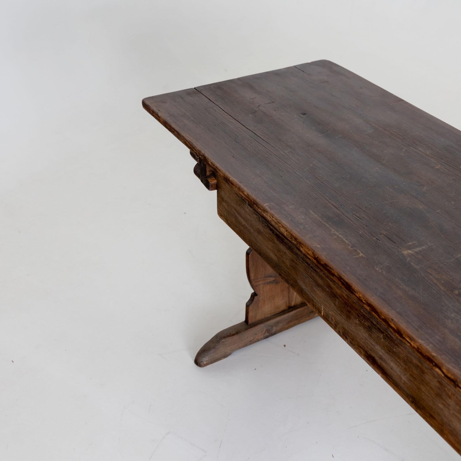 Large dining table with cut-out sides as legs and a wide board as strutting. The rectangular table top has an authentic patina. A large drawer serves as storage space.