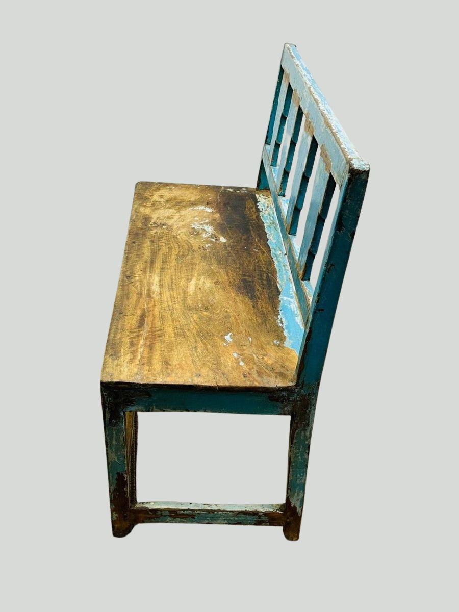 Diese rustikale Holzbank in Used-Optik hat eine auffallend blaue Lackierung mit einer gealterten Patina, die jedem Raum einen Vintage-Charakter verleiht. Die Rückenlehne ist mit einem einzigartigen geometrischen Ausschnitt versehen, der die Ästhetik