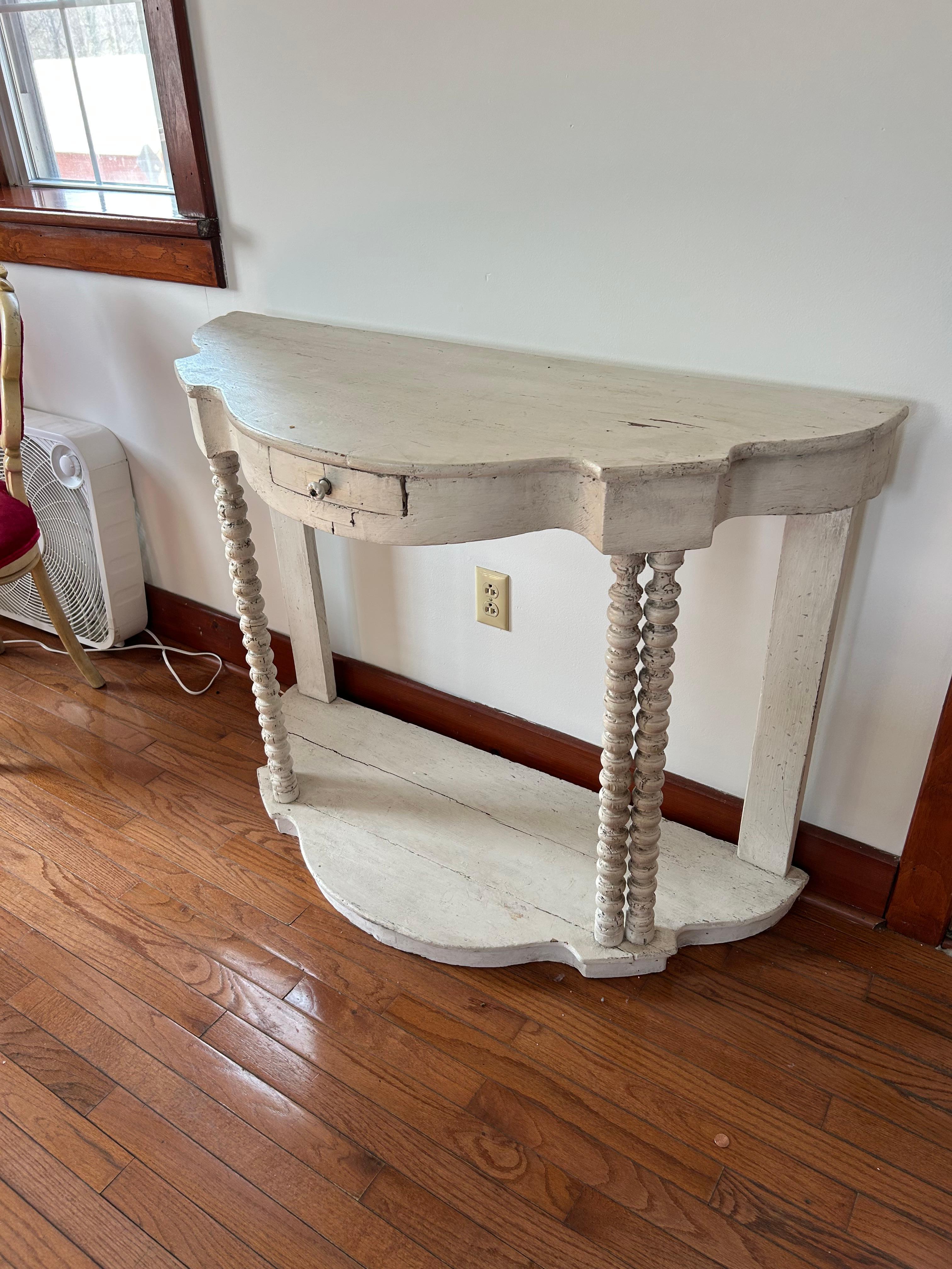 Charmante console démilune peinte en blanc vieilli avec un seul tiroir et de charmants pieds en fuseau qui se terminent par une base d'étagère inférieure.
Le look shabby chic est intemporel.

(Peintre)