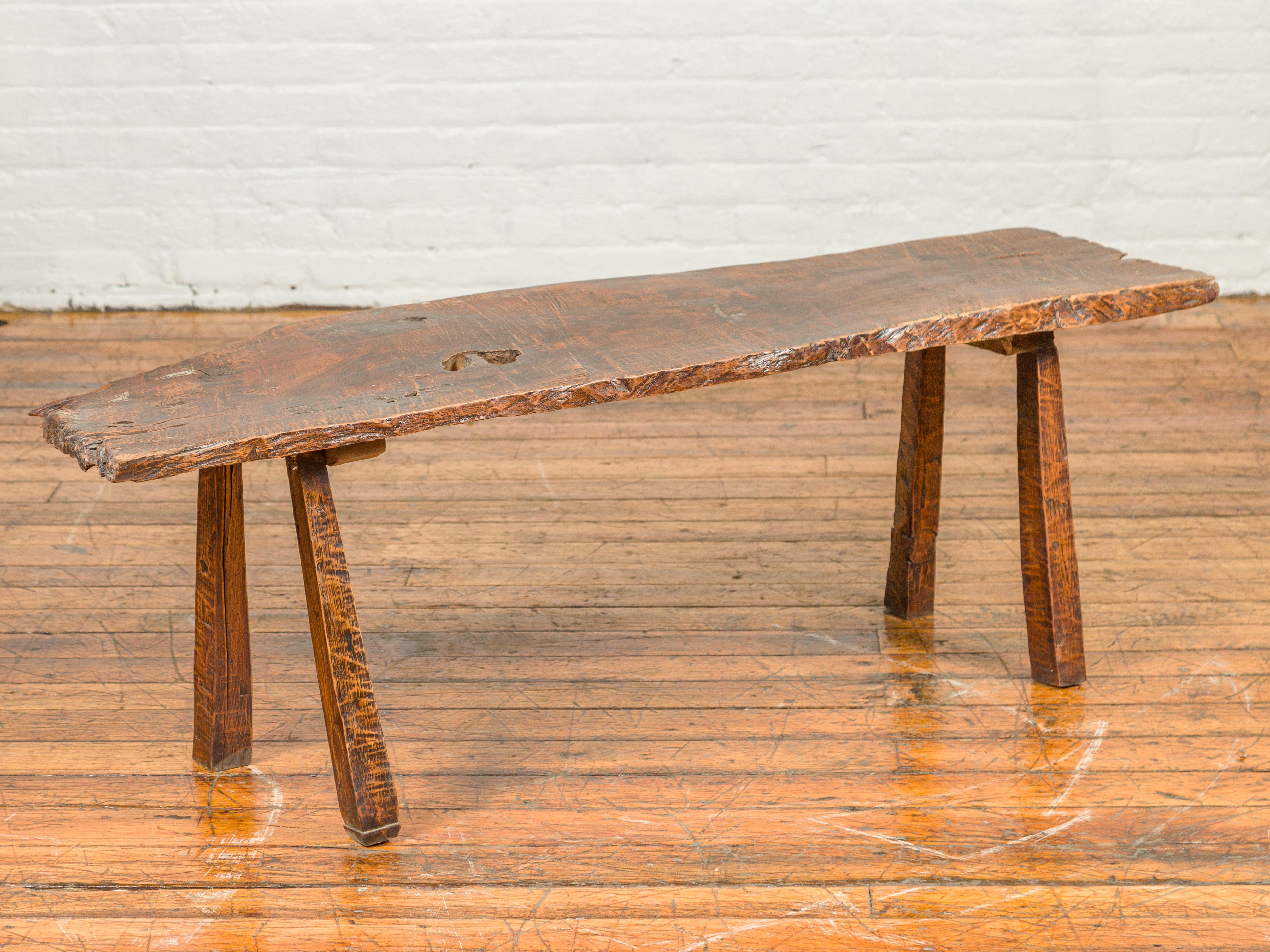 A rustic driftwood Indonesian bench with weathered appearance and splaying legs. Charming is with its worn patina and its uneven lines, this rustic driftwood bench features an irregular top sitting above four simple, slightly splaying legs. Placed