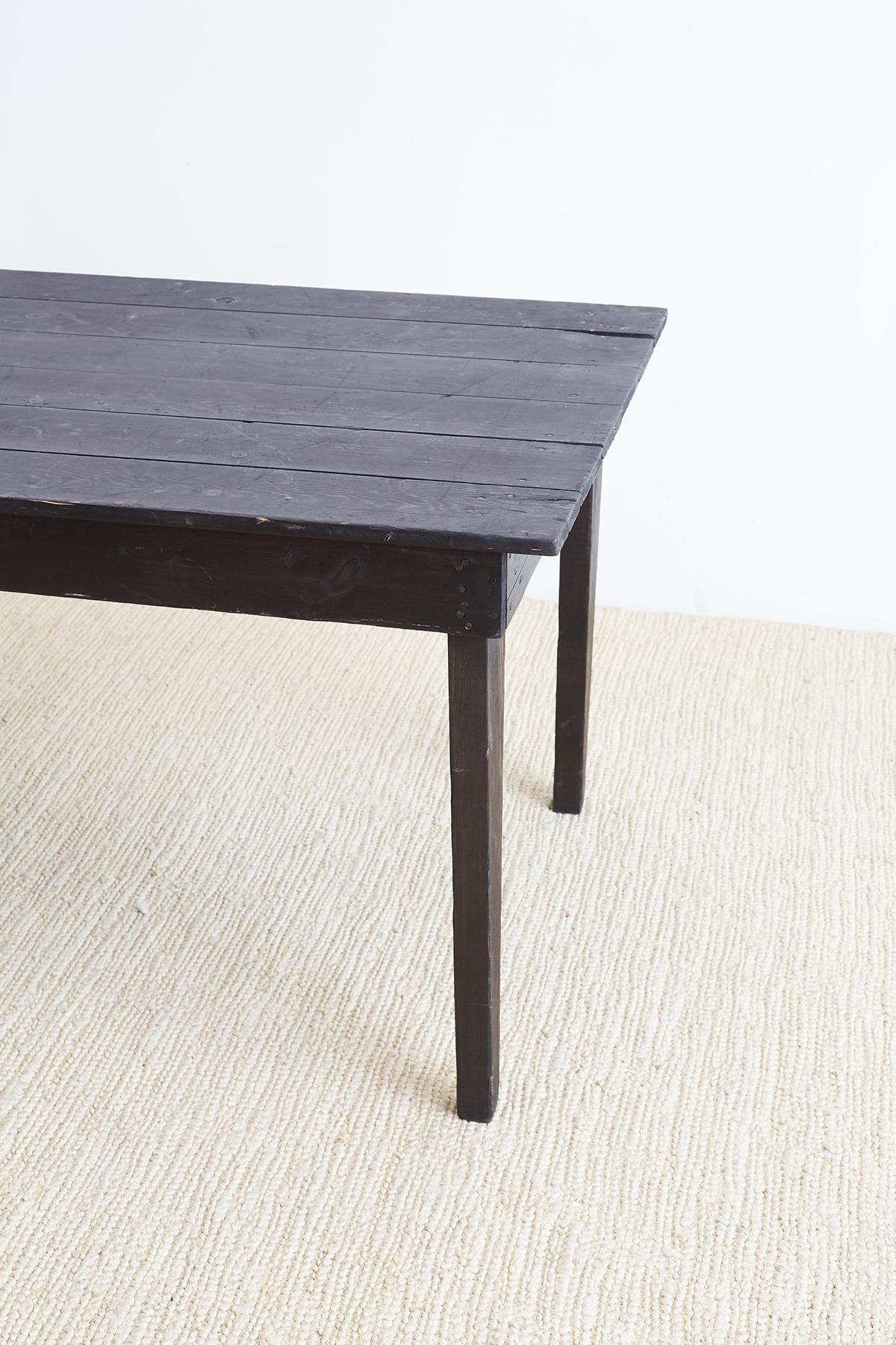 American rustic pine farmhouse dining table featuring a dark ebonized finish. Minimalist style plank top table supported by tapered legs. The top is made of a ship lap style wood similar to barn siding with grooves. The finish is a dark charcoal