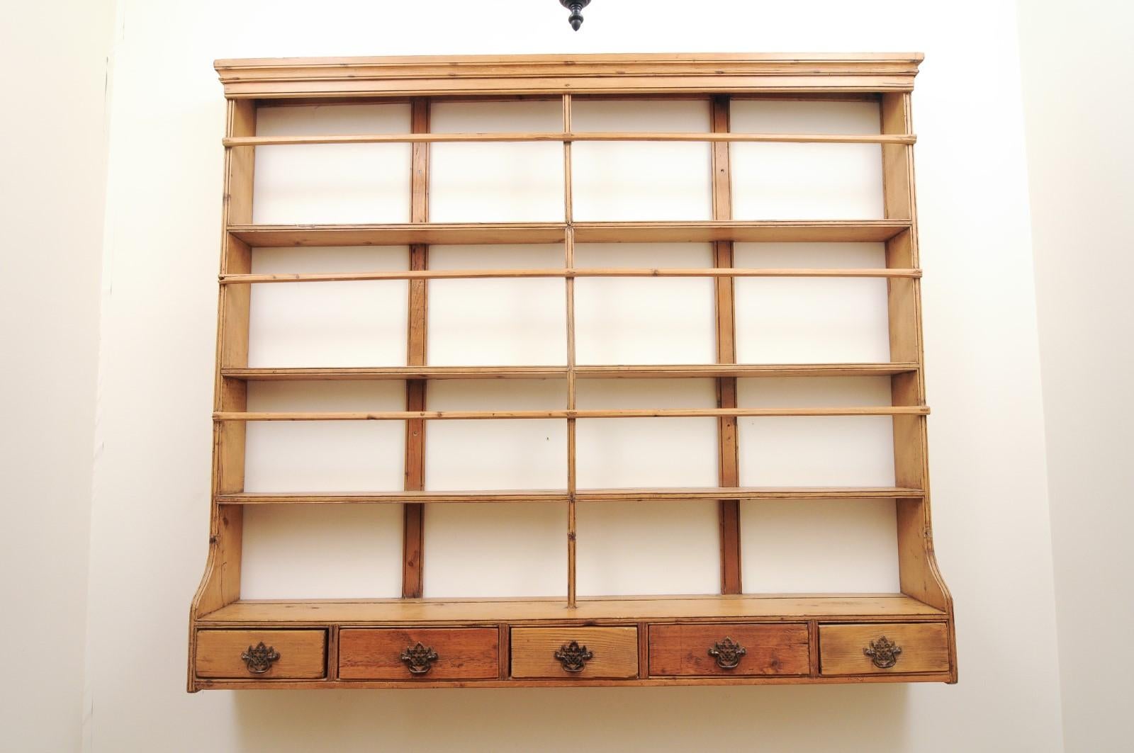 An English Georgian pine wall plate rack from the early 19th century, with low drawers. Created in England at the beginning of King George IV's reign, this wall rack features a linear silhouette perfectly complimented by a rustic appearance. A