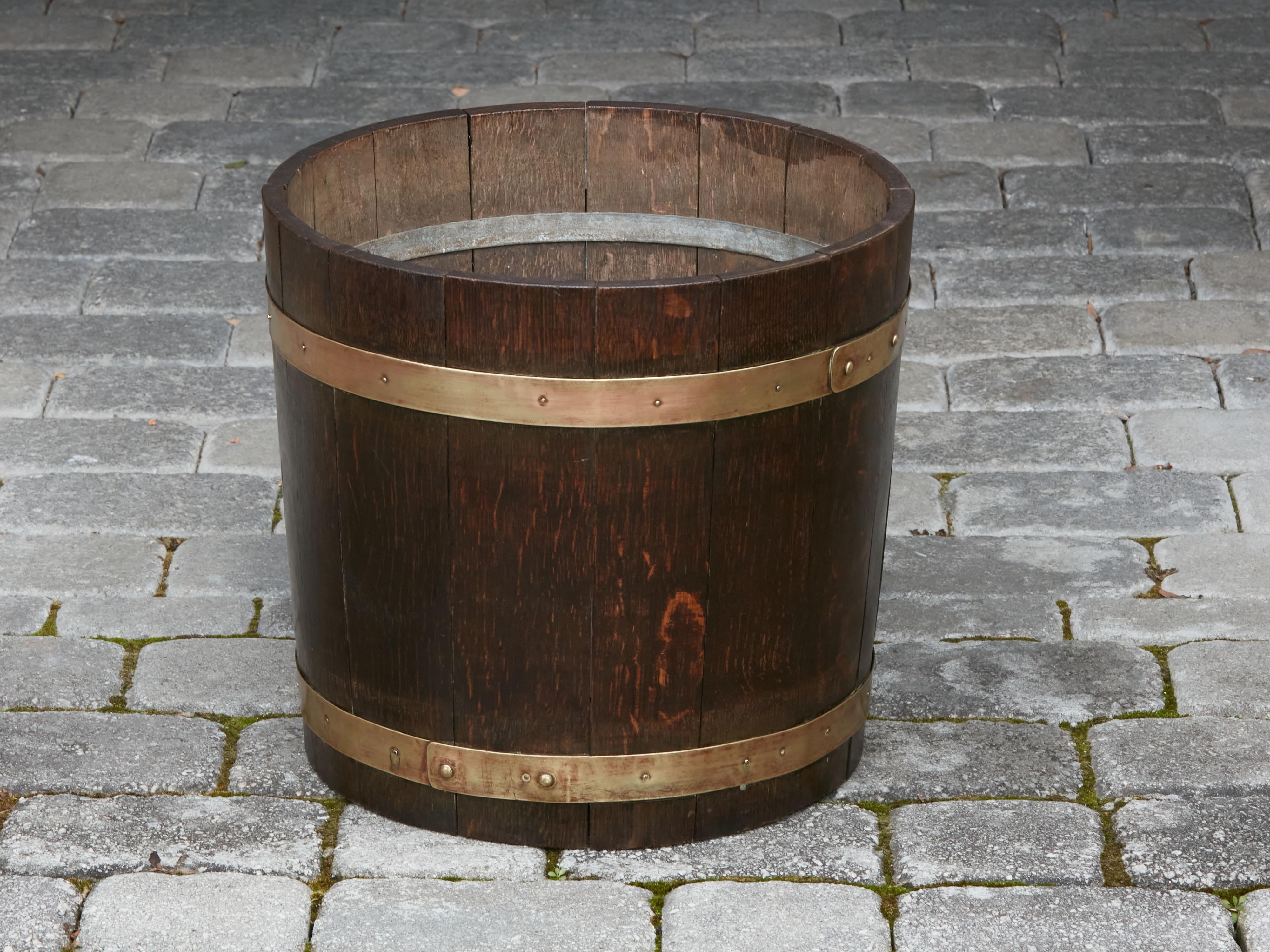 An English rustic oak bucket from the early 20th century, with brass braces. Created in England during the Turn of the Century, this oak bucket features a wooden slightly tapering structure strengthened with horizontal brass braces. With its clean