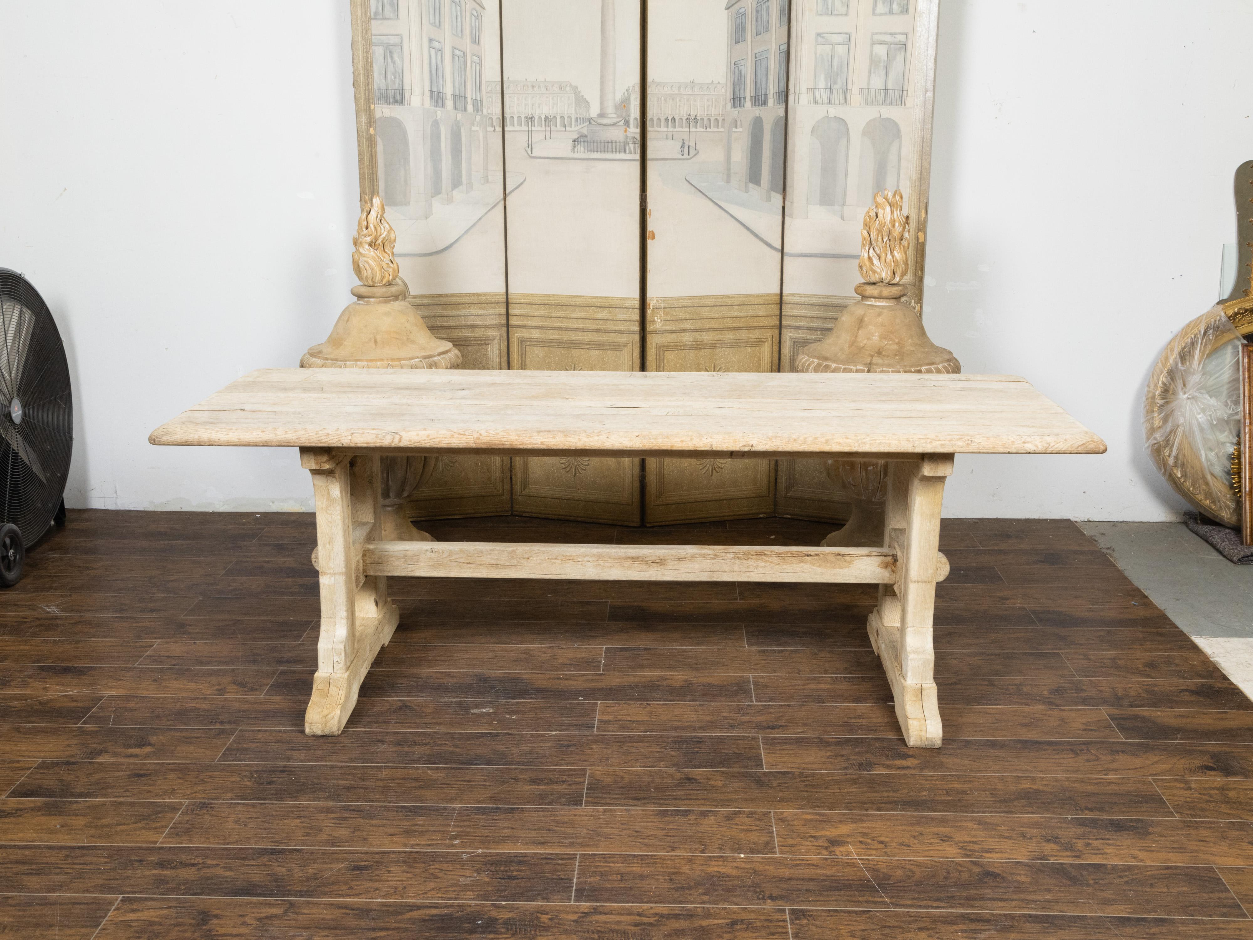 A rustic English natural wood farm table from the 19th century, with trestle base and weathered patina. Created in England during the 19th century, this farm table charms us with its rustic presence and natural grain. The table features a