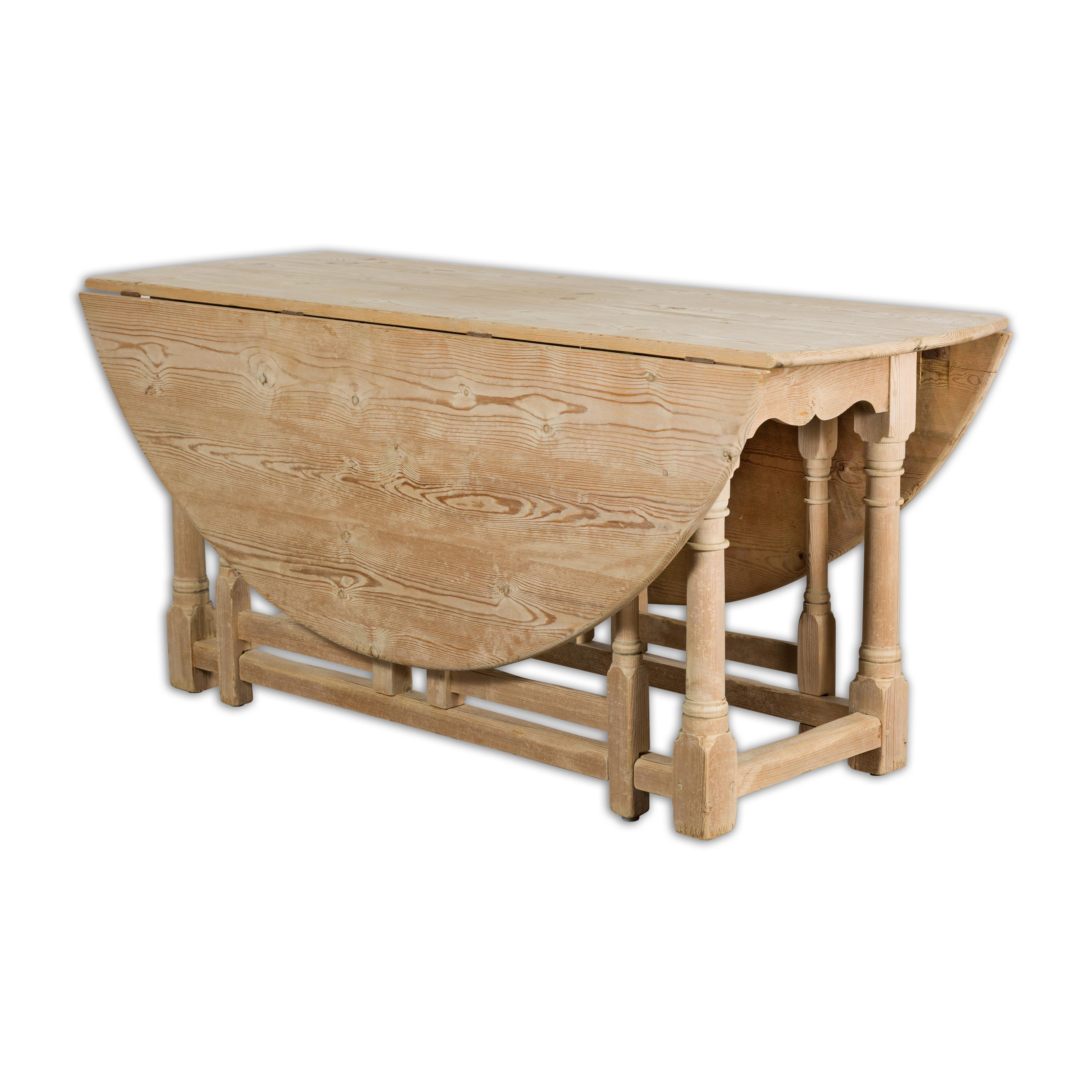A rustic English pine drop leaf table from the 19th century with round top, turned legs, carved apron, plain side stretchers and rectangular block joints. Introduce a touch of rustic charm to your home with this exquisite 19th-century English pine
