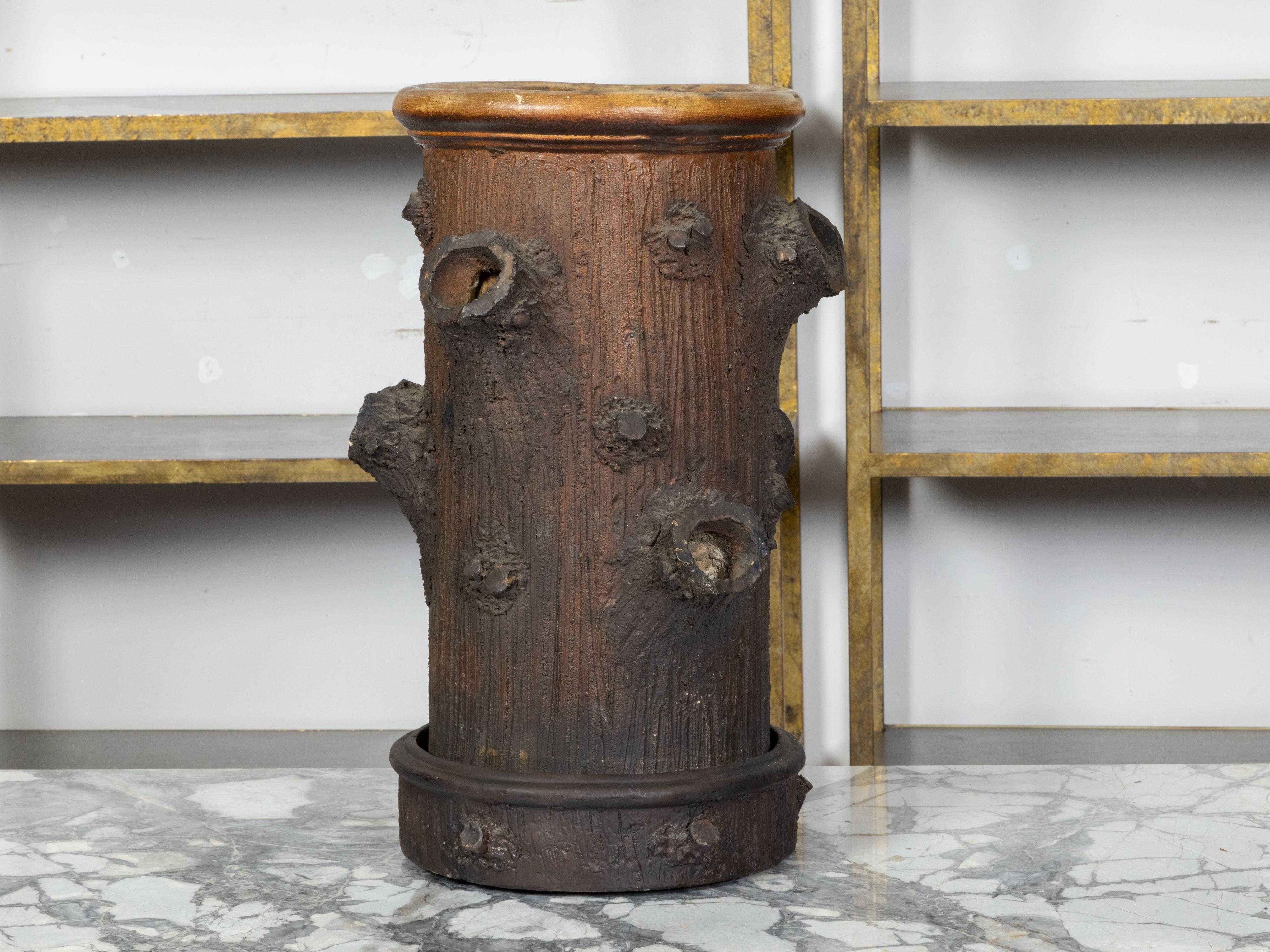 An English rustic tree trunk faux bois painted terracotta umbrella stand from the 20th century, with branch collar motifs, brown patina and drainage plate. Created in England during the 20th century, this umbrella stand charms us immediately with