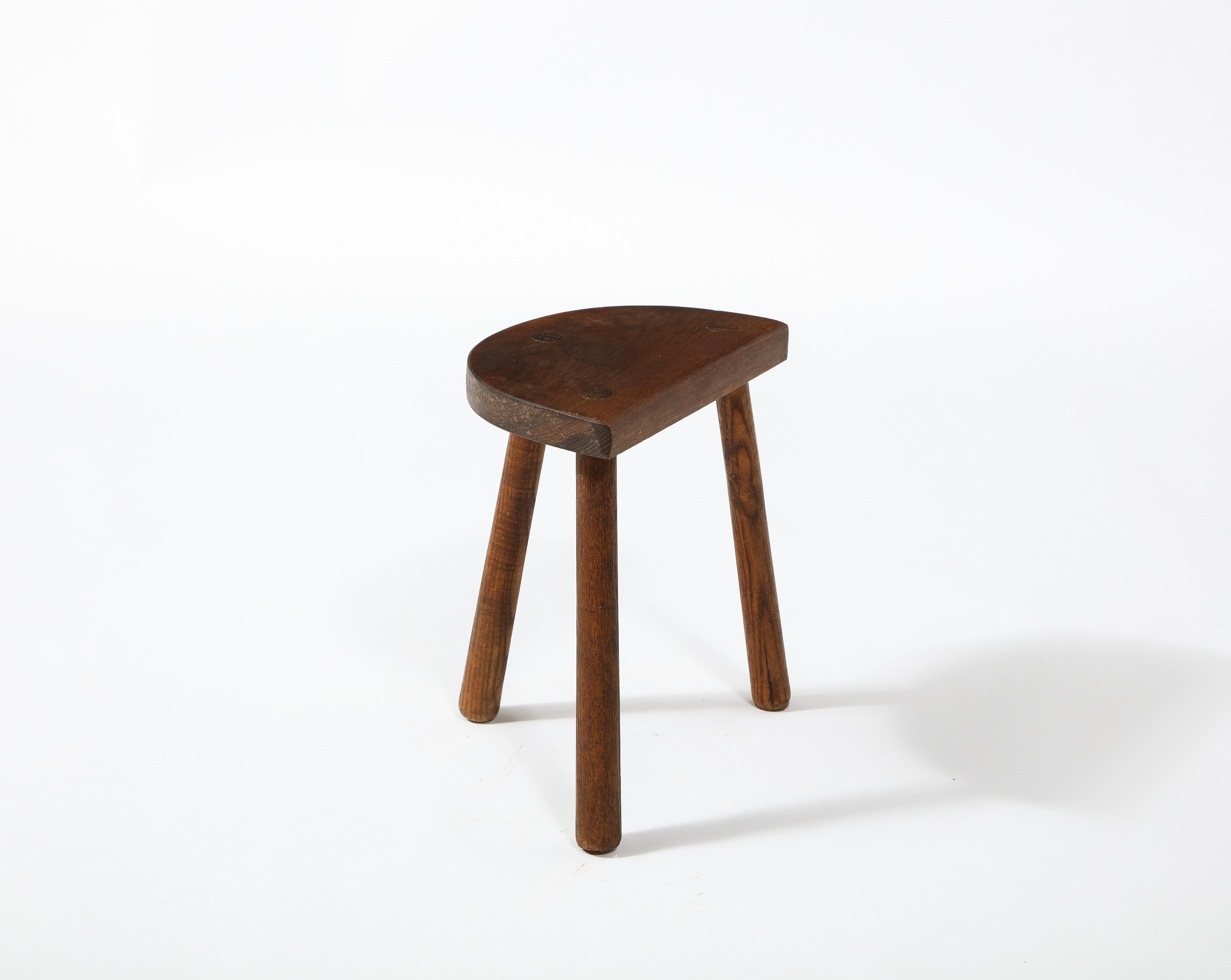 A rustic tripod farm stool with a curved seat.