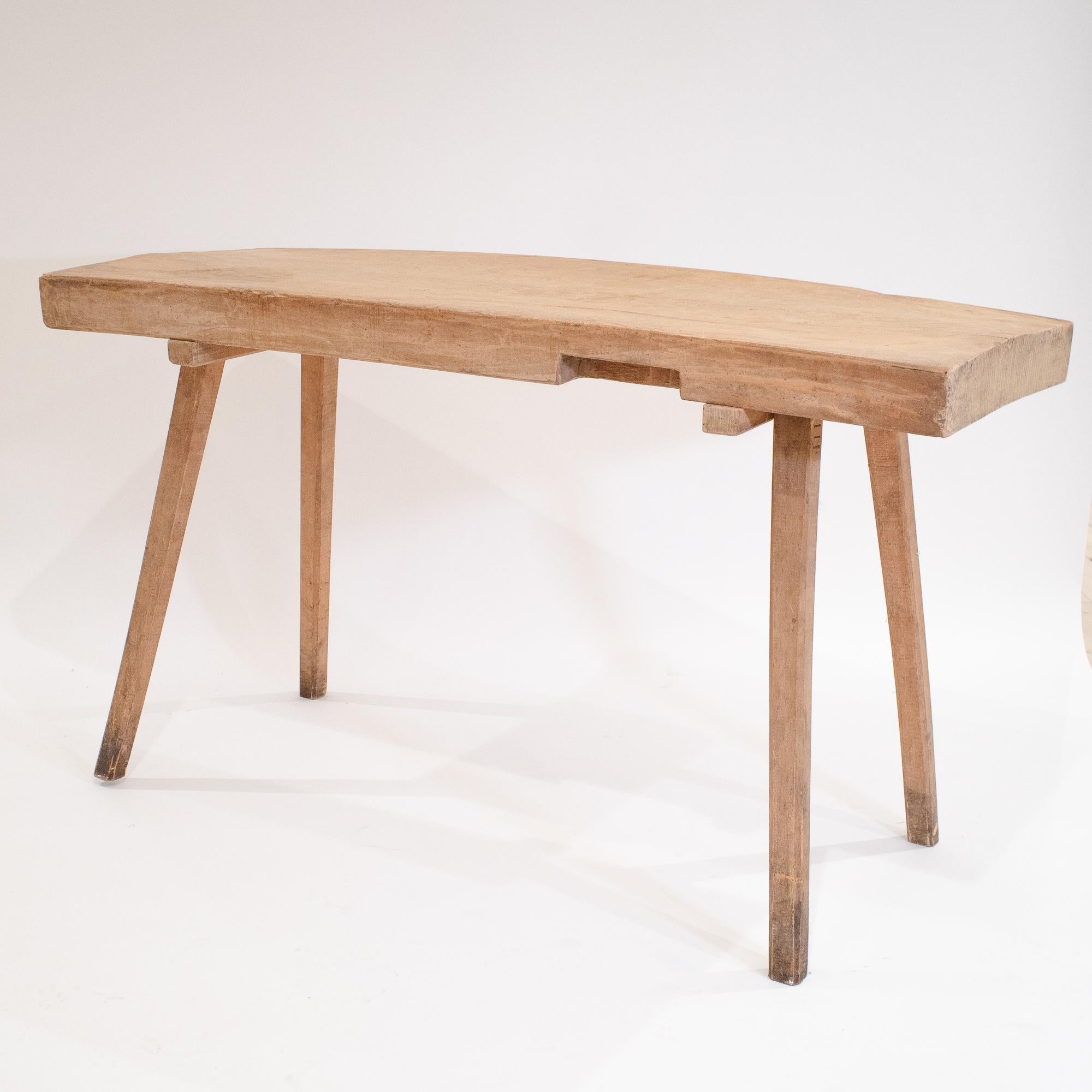 Cet établi rustique se caractérise par une substantielle dalle de bois dur massif brut, dont la forme préserve l'ordre naturel de l'arbre. La surface du plateau est pleine de caractère, avec des motifs de grain profonds et une patine d'usage