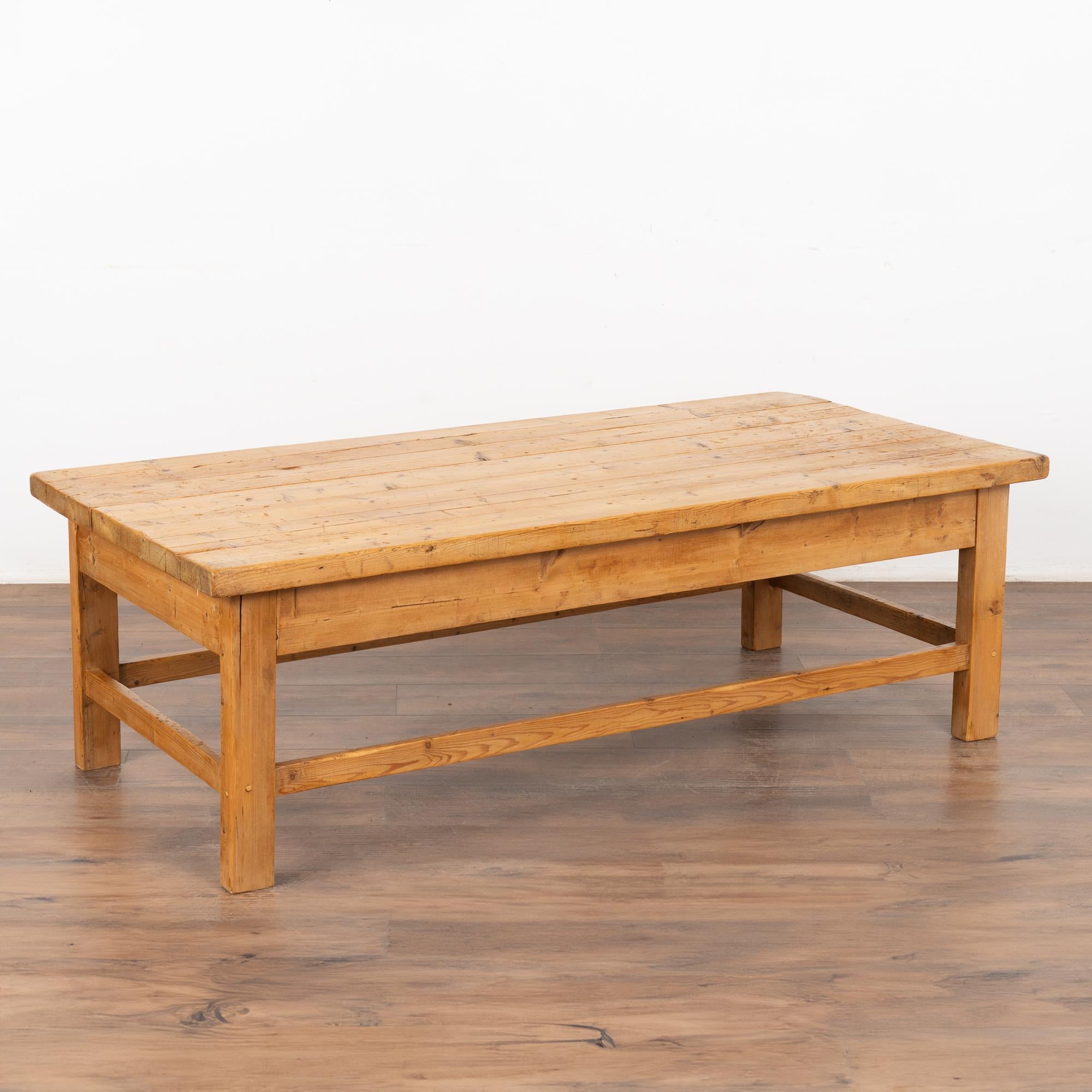 Rustic farmhouse style coffee table loaded with vintage character.
The plank wood top is covered in scrapes, gouges, stains and old cracks acquired with 100 years of use as a work table. 
Restored and waxed, this coffee table is strong, sturdy and