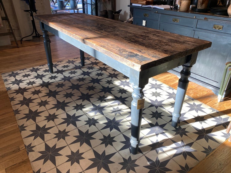 The perfect vintage dining table for a home that welcomes a rustic decor and a deeper aesthetic. The legs of the table are painted in a blackish blue hue, while the top shows wear of multiple layers of black paint.