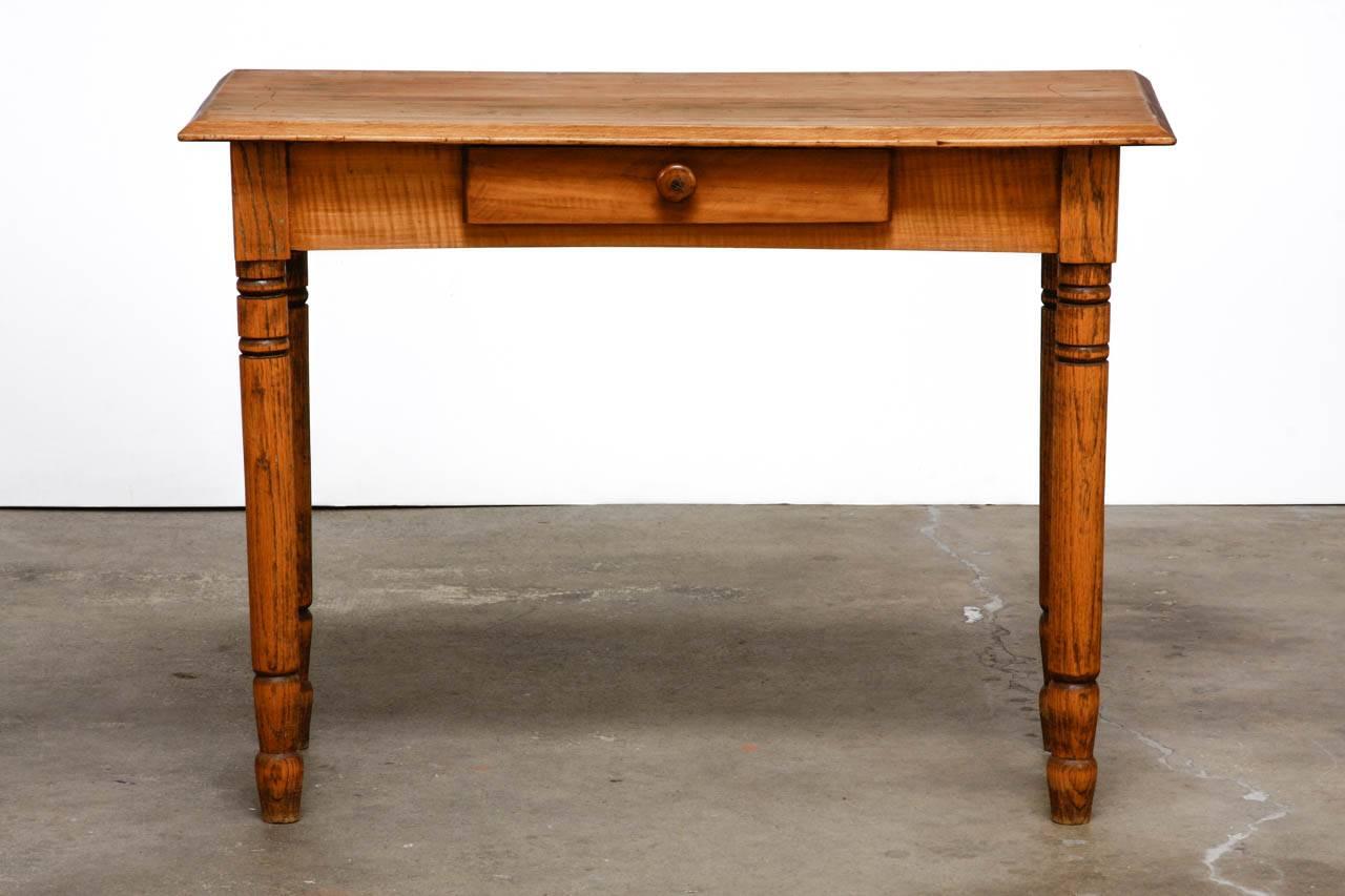 Rustic farmhouse oak work table or console fronted by a single drawer. The work surface has a beveled edge and the case is supported by round turned legs. Each leg is decorated with rings and spade style peg feet. This table could also serve as a