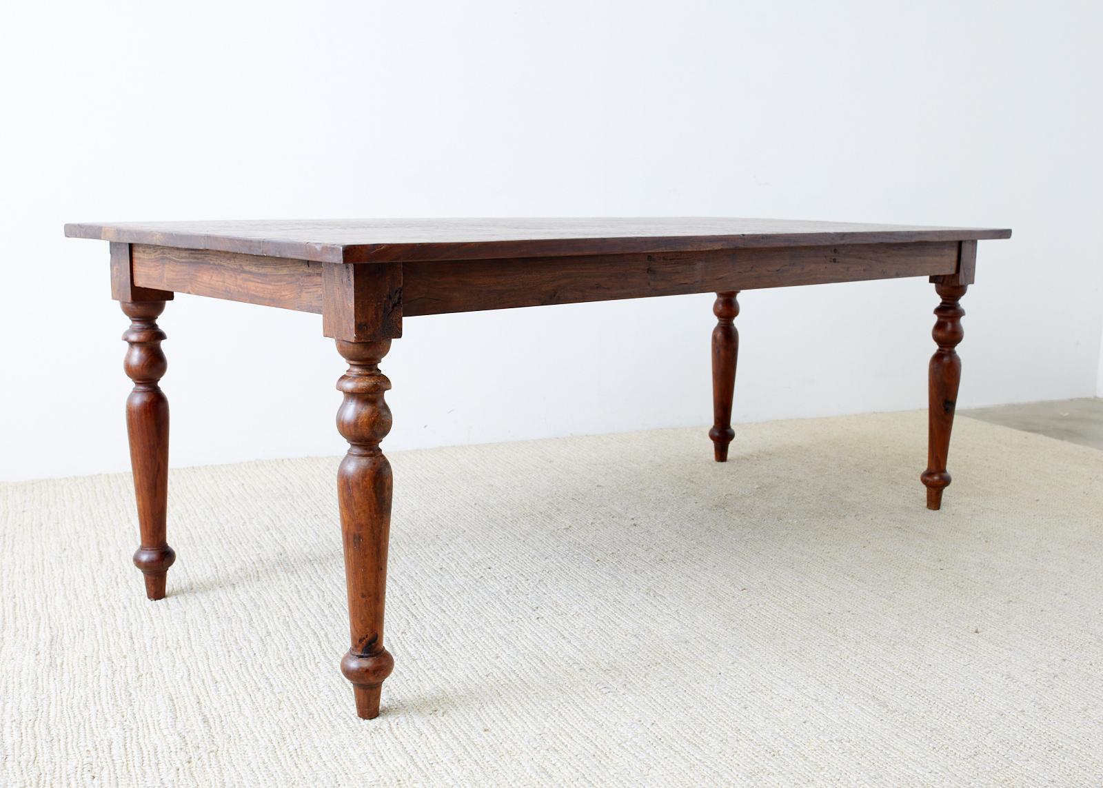 Gorgeous hardwood dining table constructed from teak or rosewood. Made in a rustic farmhouse style from hand-hewn planks 1 inch thick with a beautiful soft chink groove finish on the top. Very heavy and solid supported by elegant turned legs. The