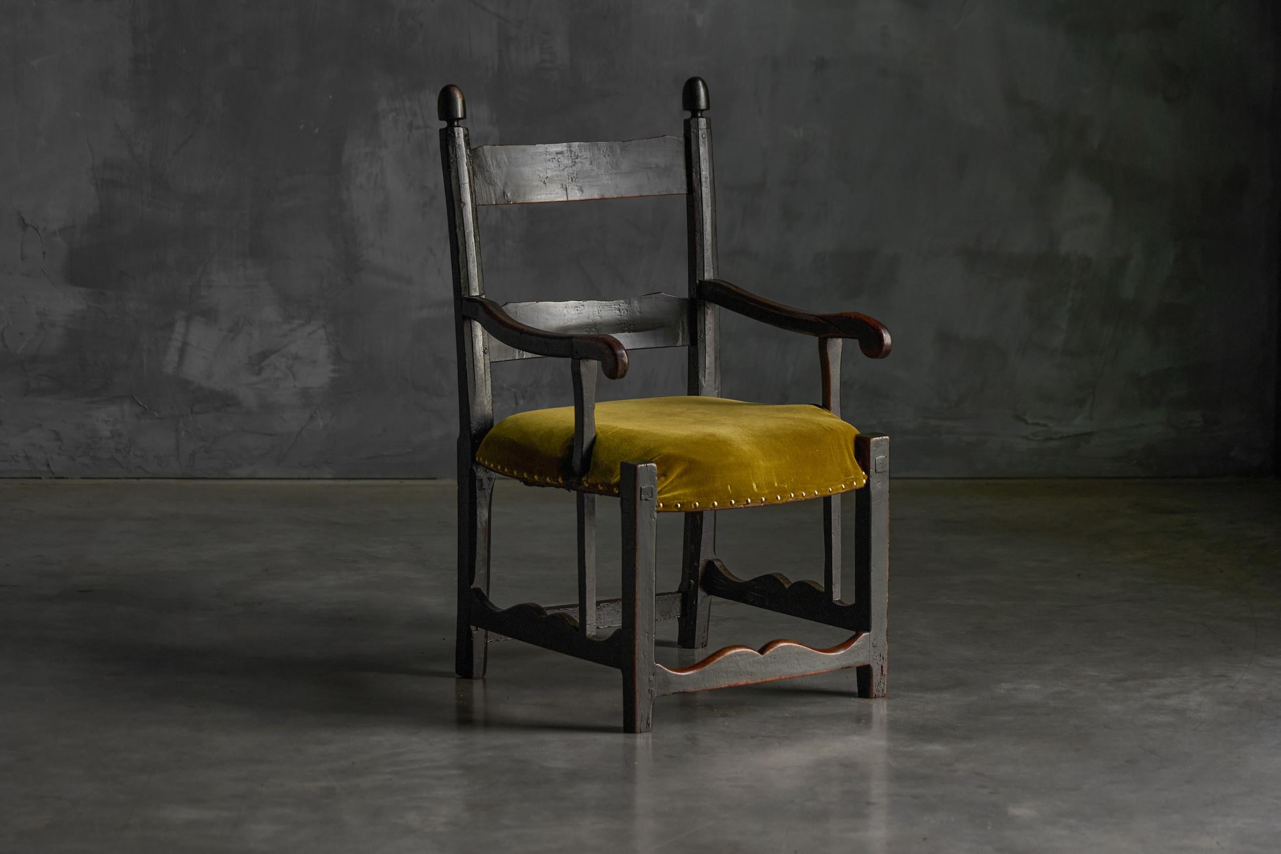 Ce fauteuil alsacien du XIXe siècle présente un cadre en bois teinté foncé, typique de l'artisanat régional. Le dossier comprend deux lattes horizontales surmontées d'épis de faîtage arrondis, ce qui ajoute à son charme rustique. Les accoudoirs