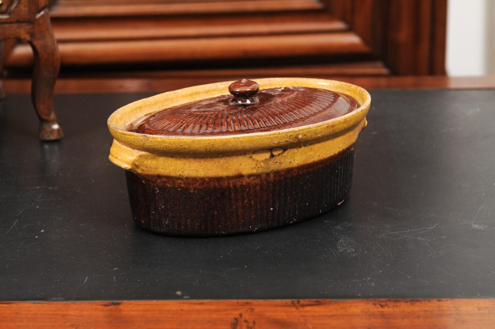 A rustic French covered pâté tureen from the 19th century with brown glaze. Created in France during the 19th century, this terrine features a traditional oval body topped with a lid and flanked with slight handles. Showcasing a brown and gold