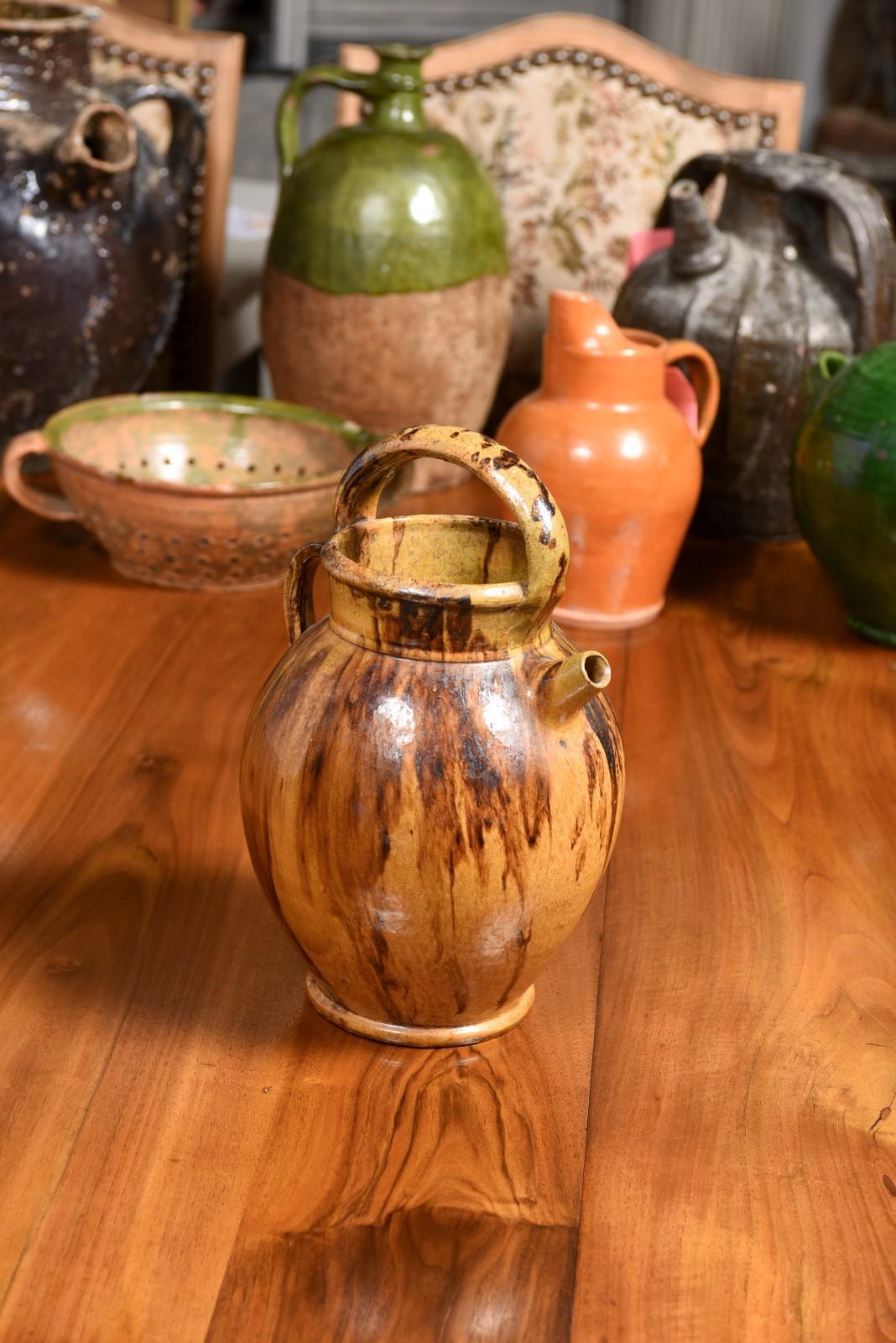 Rustic French 19th century pottery olive oil jug with front spout, large upper handle and back one. This 19th-century rustic French pottery olive oil jug exudes an irresistible old-world allure, and stands as a testament to a bygone era, making it a