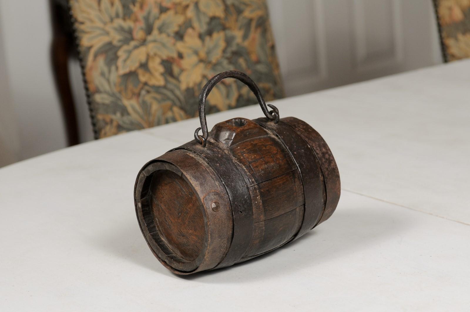 A French petite barrel from the 19th century, with iron handle and accents. Created in France during the 19th century, this decorative barrel charms us with its petite proportions and nicely rustic appearance. Showcasing a brown slatted structure