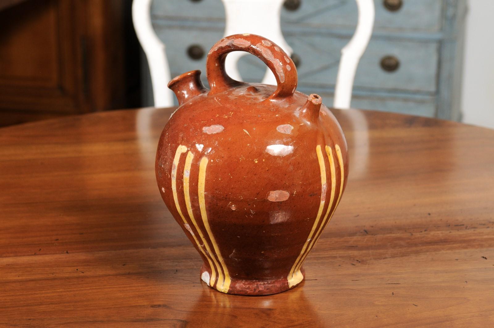 A rustic French pottery jug from the 19th century, with russet ground and yellow glazed stripes. Created in France during the 19th century, this pottery jug charms us with its generous lines and complimenting colors. Showcasing a rust toned ground,