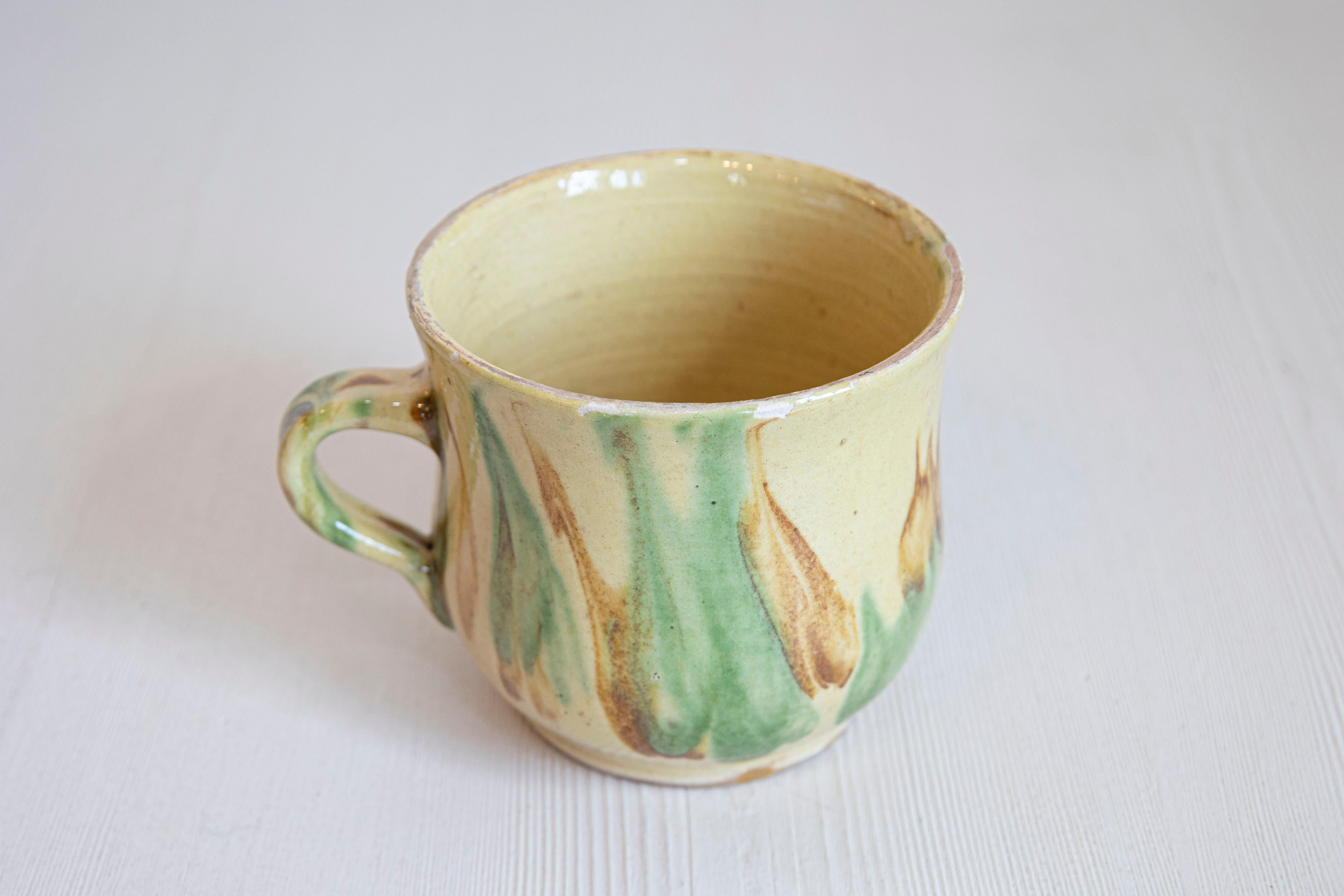 Mug en poterie française du 19e siècle, avec une glaçure jaune, verte et rouille. Créée en France au cours du XIXe siècle, cette tasse en poterie présente un corps cylindrique et incurvé, avec un fond jaune orné d'une glaçure verte et rouille.