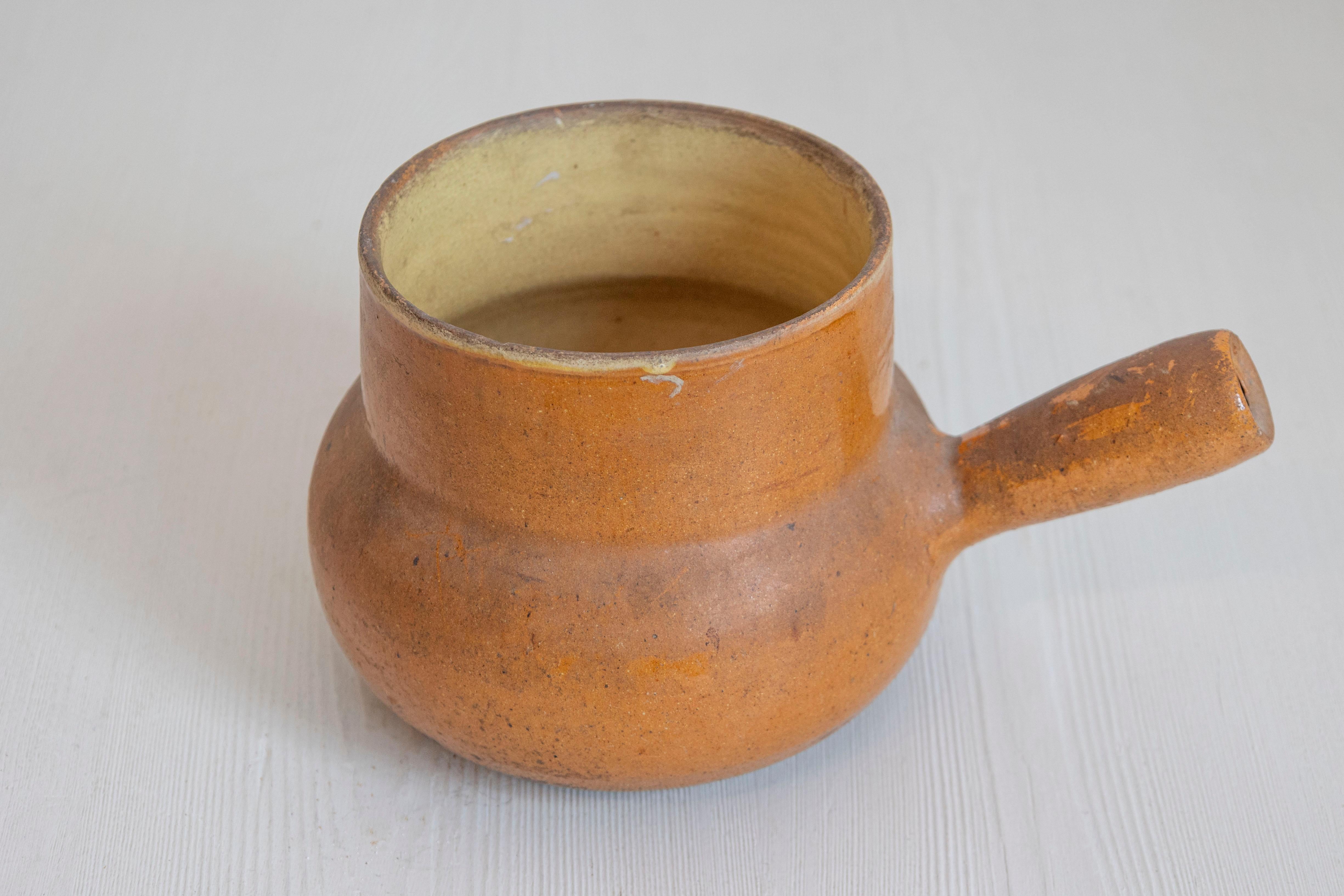 Poterie française rustique du XIXe siècle, à glaçure brune et à anse droite. Créée en France au cours du XIXe siècle, cette poterie présente un corps circulaire à glaçure brune, joliment patiné par les intempéries, relié à une anse droite. Un