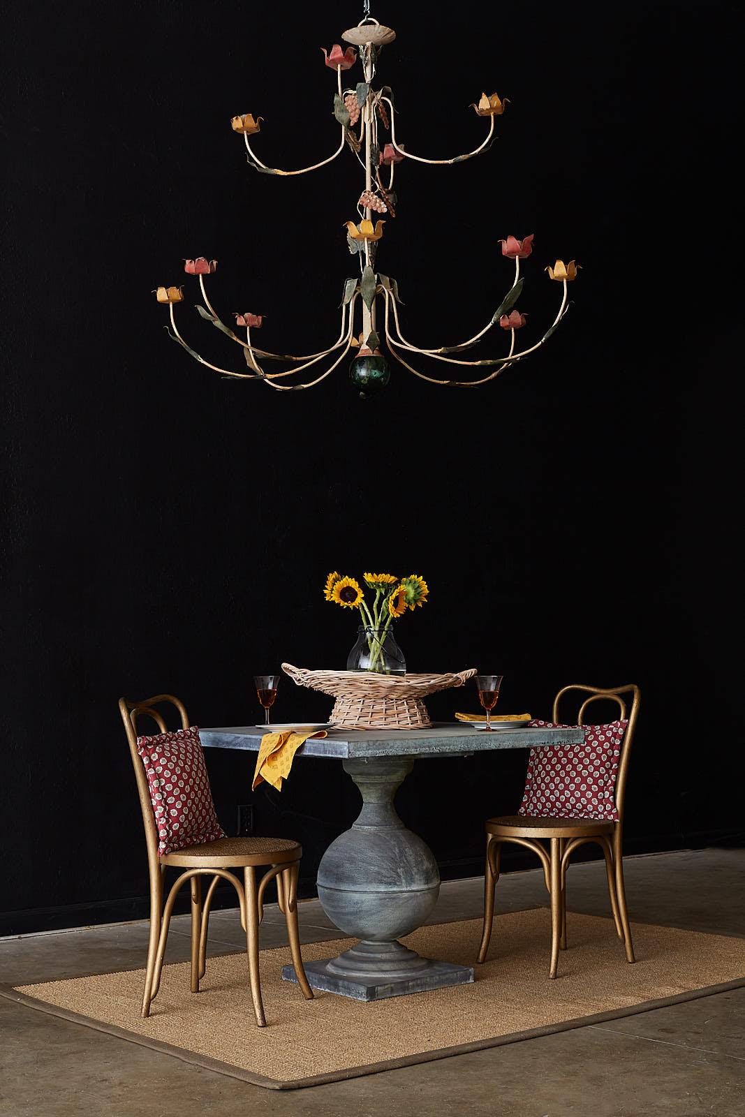 Whimsical French painted iron twelve-light candle chandelier. Features twelve curved arms with yellow and red floral motif ends. The flower petal bobeche are scrolled on the ends. The fixture has a long column decorated with grape vine clusters and