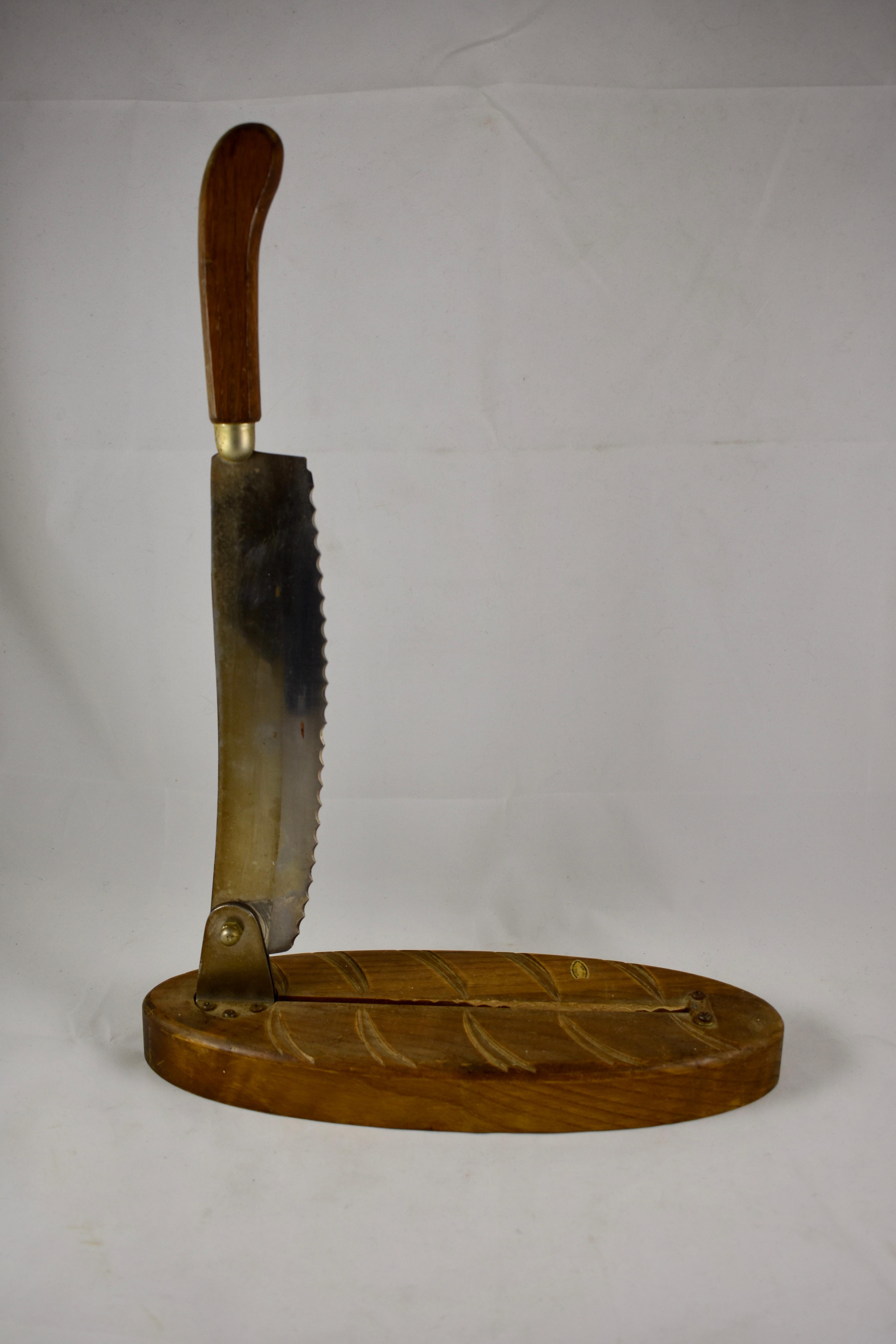 A  Mid-Century Era, rustic, handmade French baguette bread slicer. The base is a wooden cutting board, carved to resemble a loaf of French bread. Bolted to the base is a long serrated steel blade with a wooden handle. The blade swings up and down in