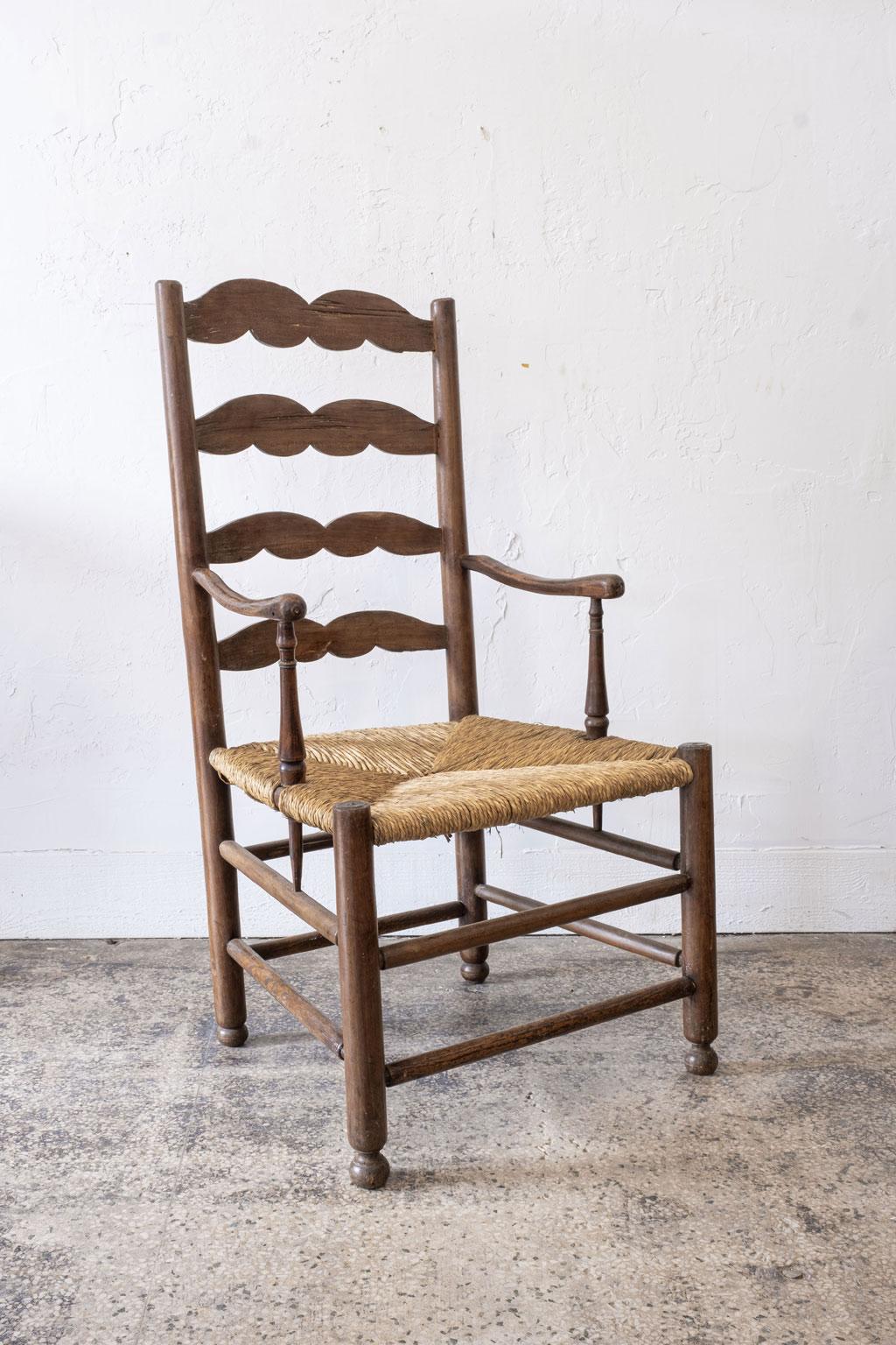 Rustic French ladder back armchair, circa 1840-1860. The shape of the scrolled ladder back slats and delicately carved arms of this chair are characteristic of furniture from the Southwest region of France. The rush seat has a beautiful patina and