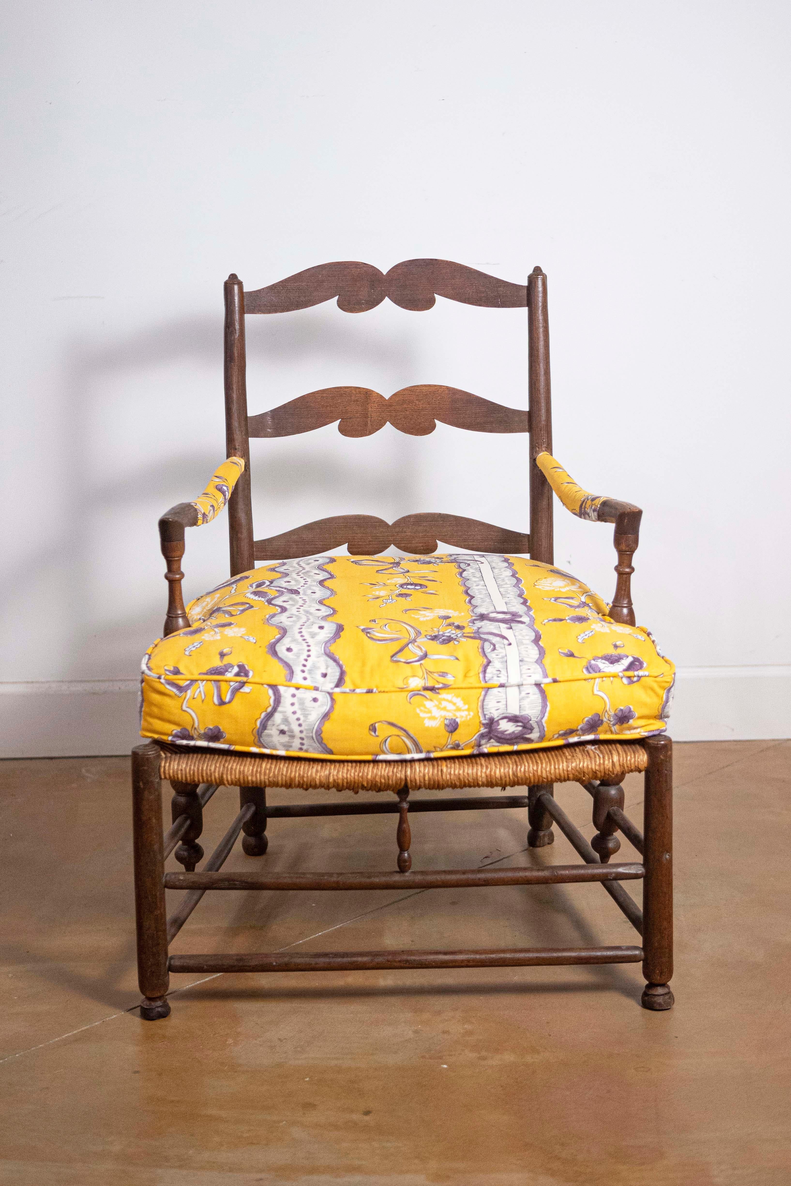 Fauteuil rustique en noyer français de la fin du XVIIIe siècle avec assise en jonc, dossier en échelle sculpté, accoudoirs incurvés et coussin rembourré. Créé en France dans les dernières années du XVIIIe siècle, ce fauteuil en noyer nous charme par