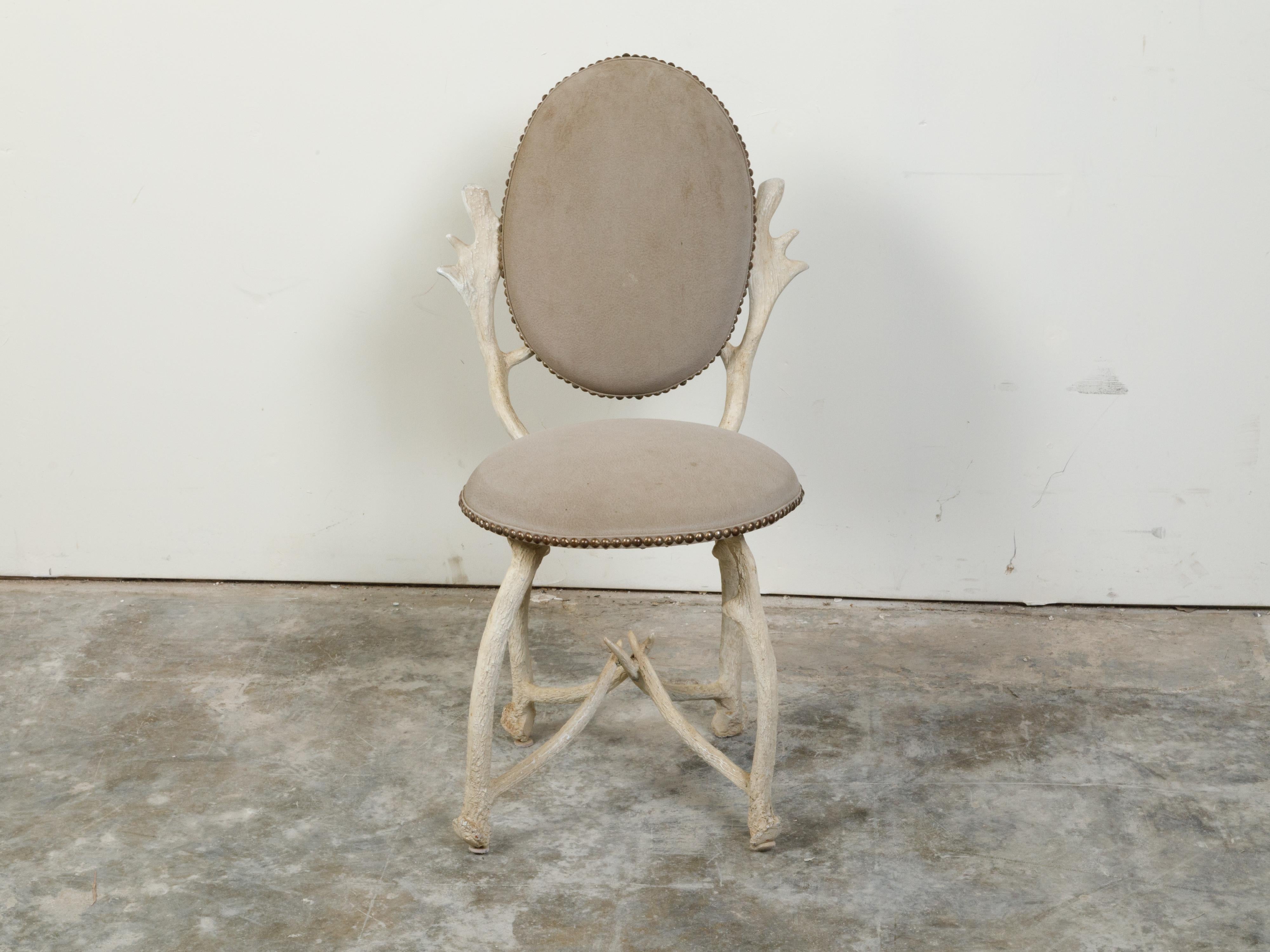 A French rustic oval back side chair from the mid 20th century, with faux antlers structure and upholstery. Created in France during the midcentury period, this rustic chair features an oval upholstered back with brass nailhead trim, sitting above
