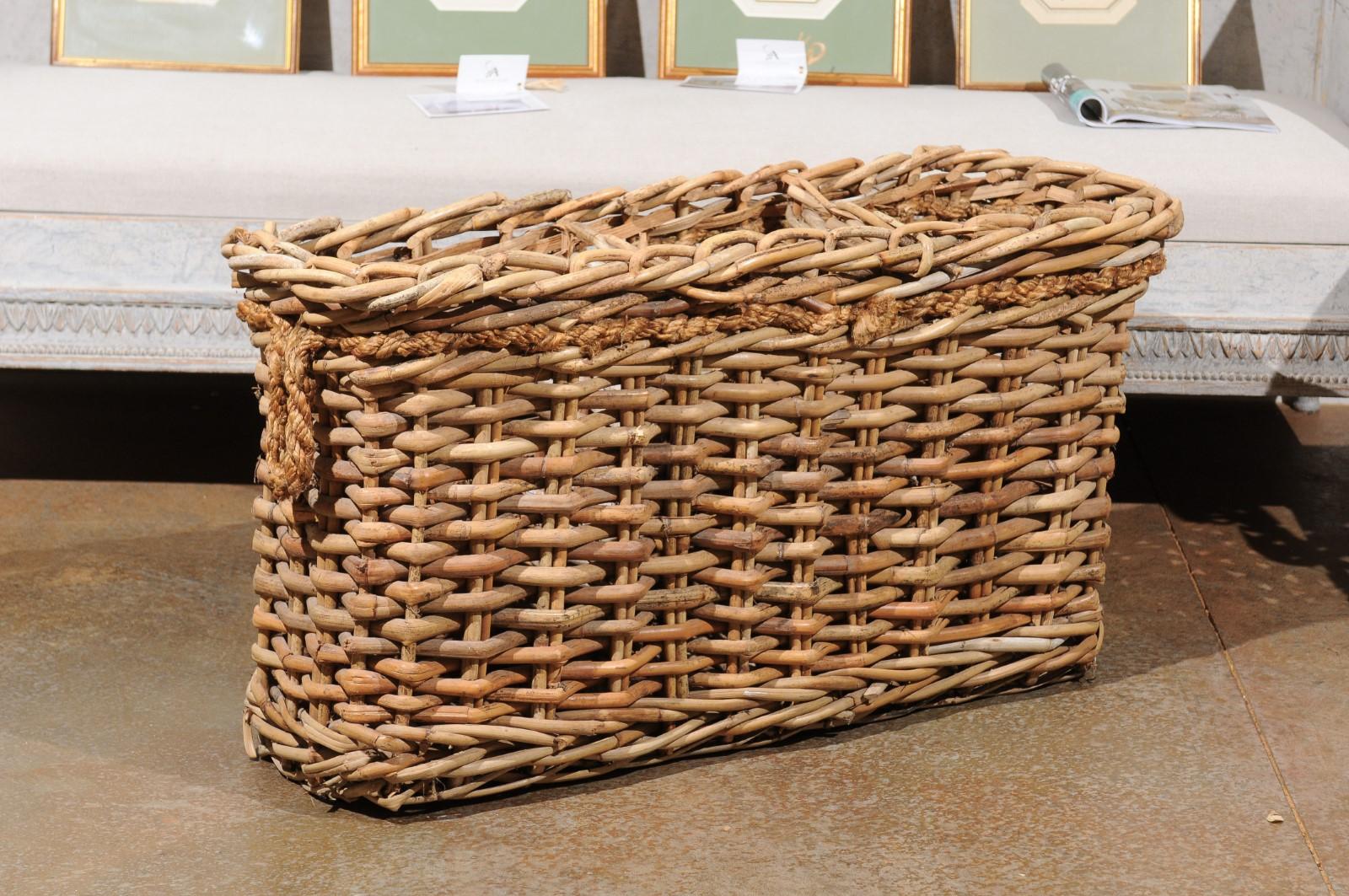 A narrow French rectangular wicker basket from the 20th century, with rope handles and partitions. Boasting a rustic presence, this French wicker basket features a narrow rectangular body highlighted with a rope surrounding the upper section and
