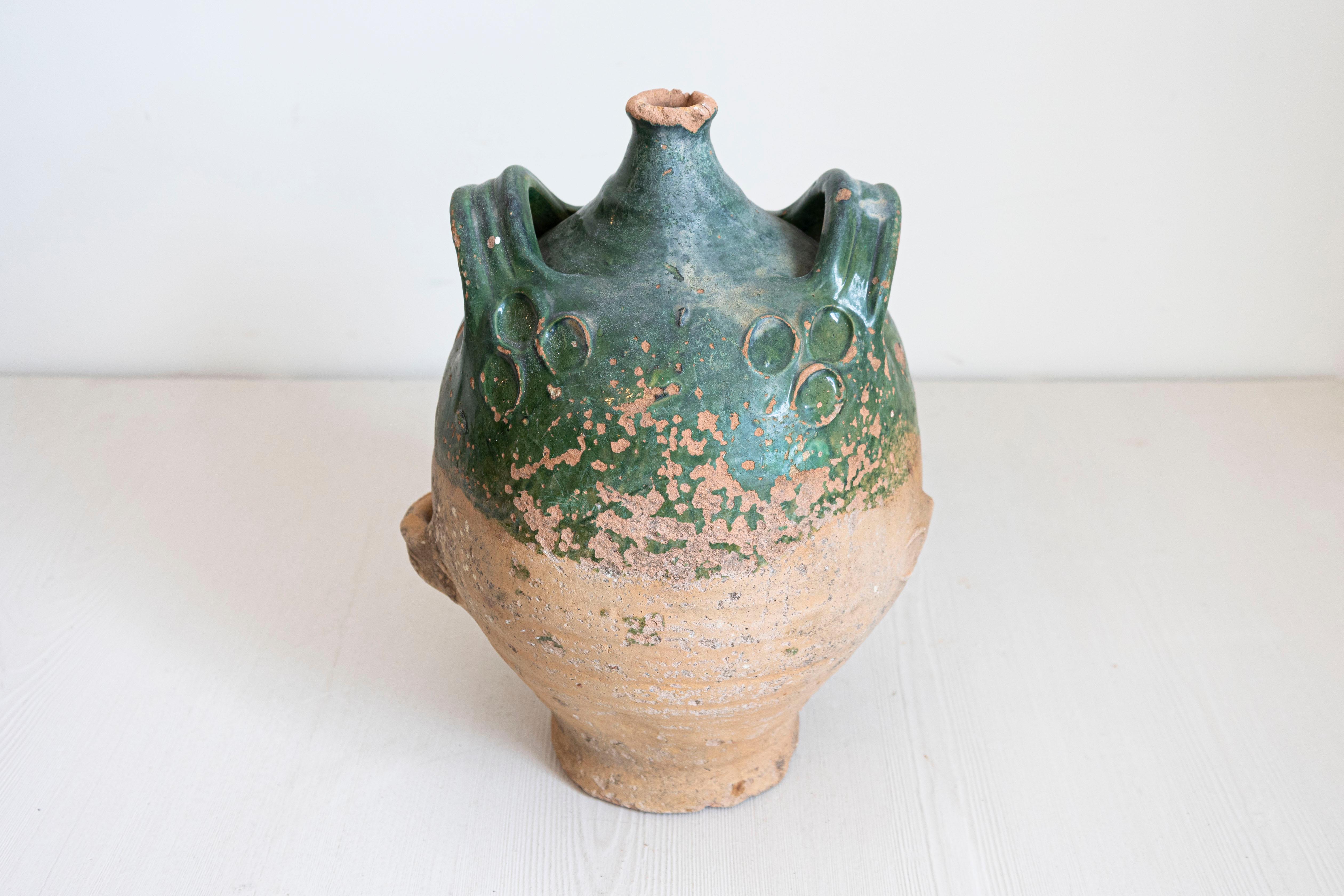 Esta jarra de aceite de oliva de cerámica rústica francesa es un testimonio de artesanía tradicional y diseño atemporal. Presenta un distintivo cuerpo bulboso adornado con sutiles motivos circulares que crean interés visual. La mitad superior está