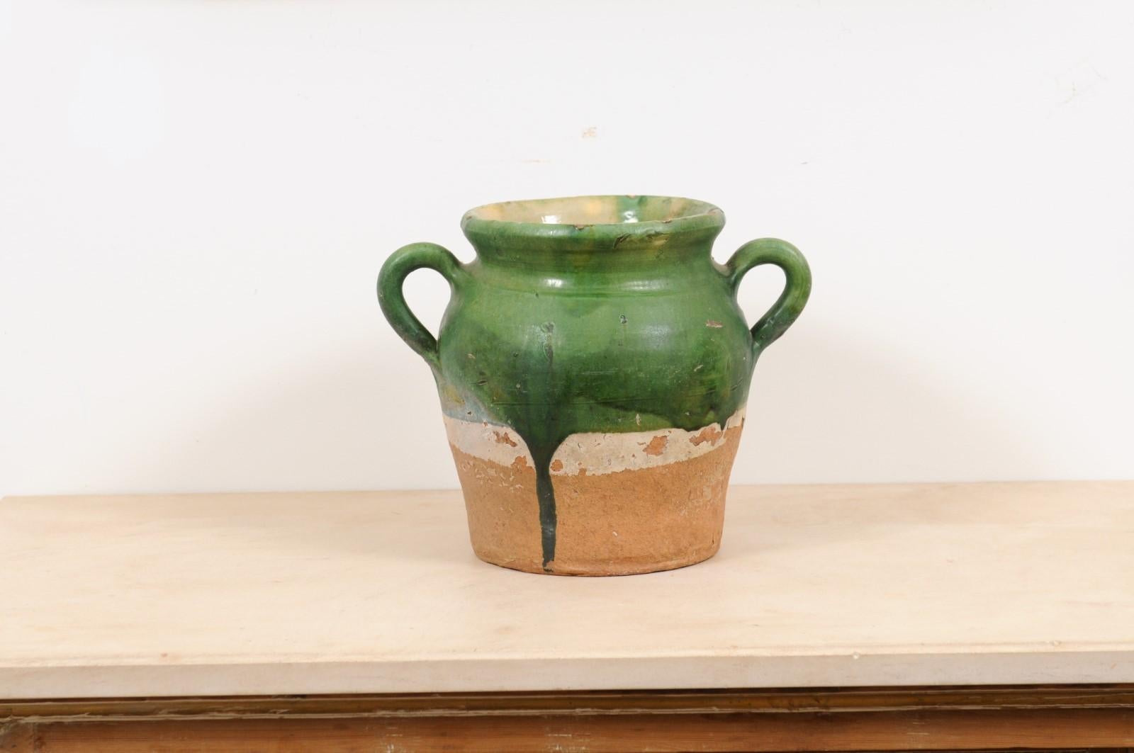 A French green glazed pottery confit pot from the mid-19th century with two handles and unglazed base. Created in France during the early years of Napoleon III's reign, this confit pot features a green glaze in its upper section dripping on the