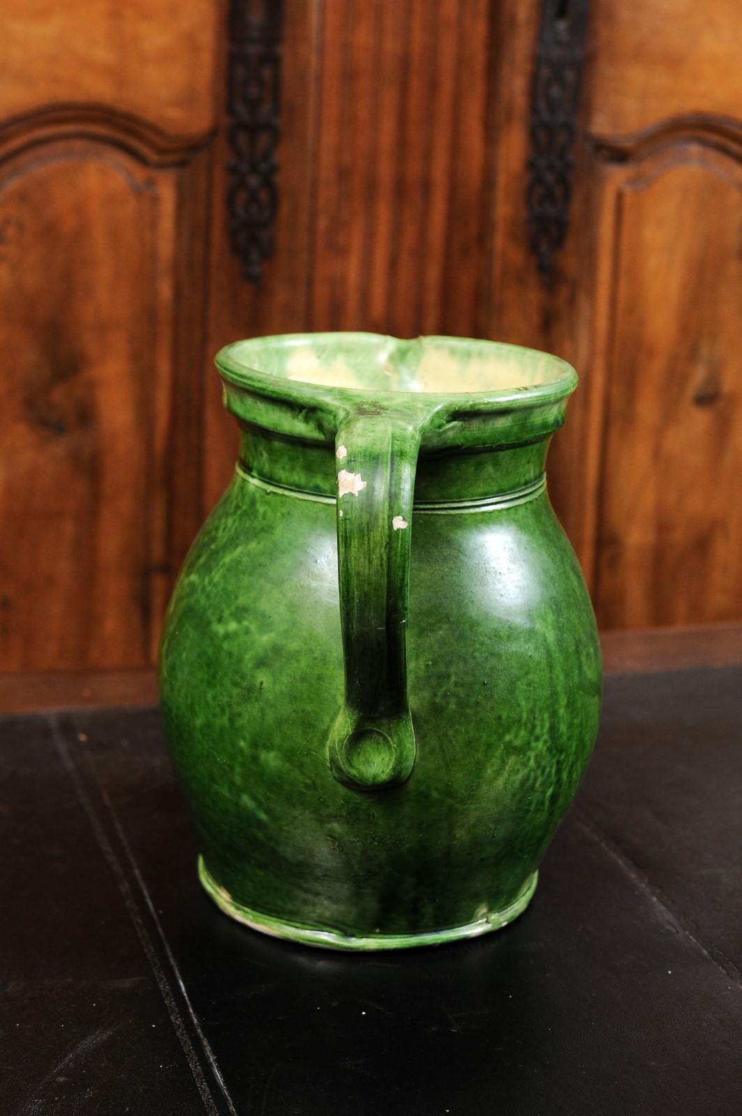 A French Provincial pitcher from the 19th century, with green glazed décor. Created in Southern France during the 19th century, this pottery pitcher features a green glazed body showcasing a back handle and front spout. Perfect to be used as a vase