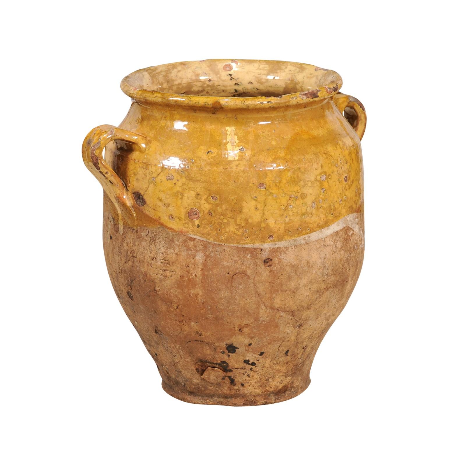 A French Provincial pot à confit pottery from the 20th century with yellow glaze, two lateral handles and rustic patina. Delve into the rustic charm and timeless beauty of this French Provincial pot à confit from the 20th century, a delightful