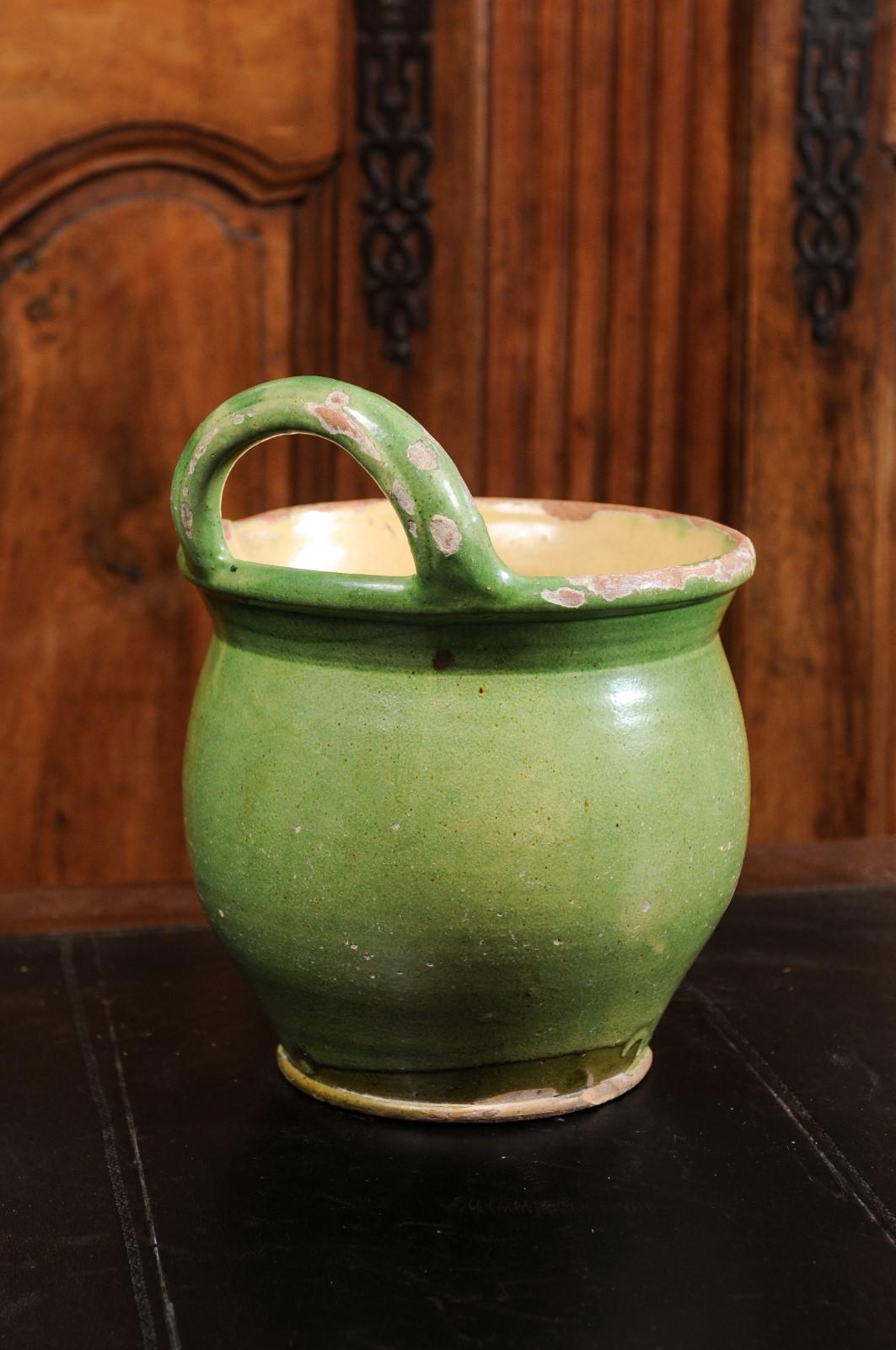 A rustic French Provincial pottery jardinière from the 19th century, with green glaze, back handle and nicely weathered patina. Created in Southern France during the 19th century, this pottery jardinière features a circular bulbous body covered with