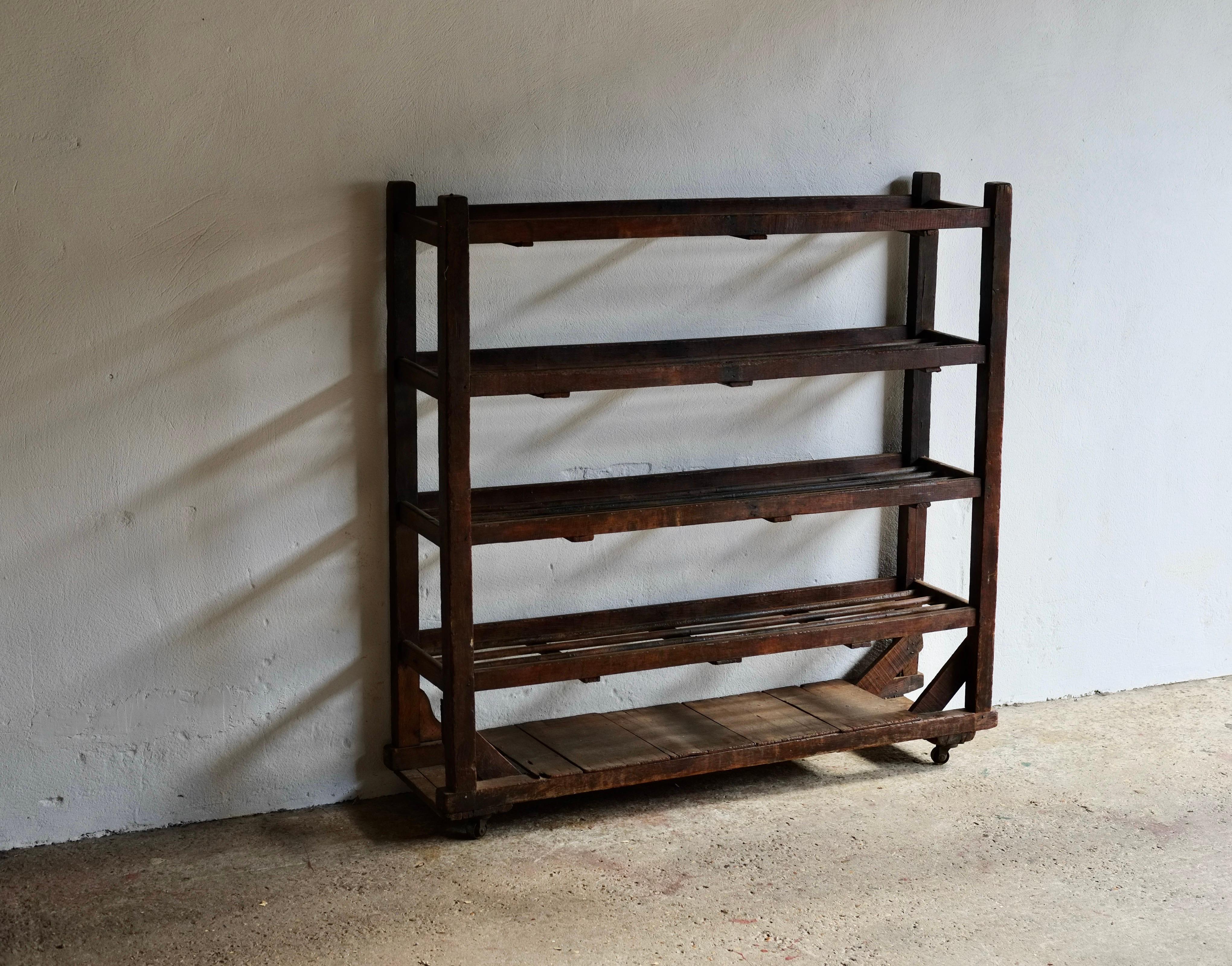 A rustic wooden French shelving unit featuring dowelled shelves raised on castors.