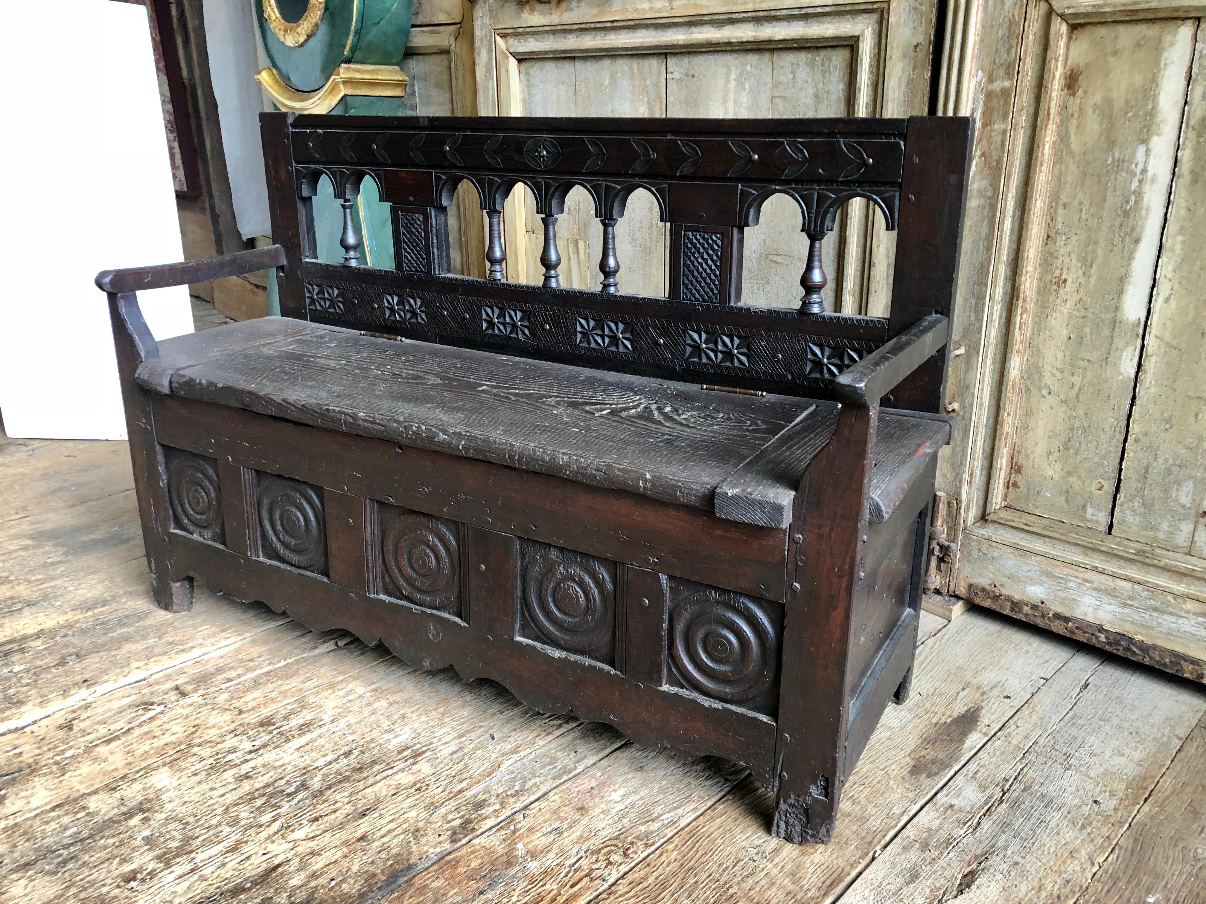 A French Country storage bench with back and arms, 18th century from Brittany France, with lift seat which hides an open compartment for shoes, umbrellas etc. Great in an entry hall or mud-room. Carved decoration on back and base with a row of