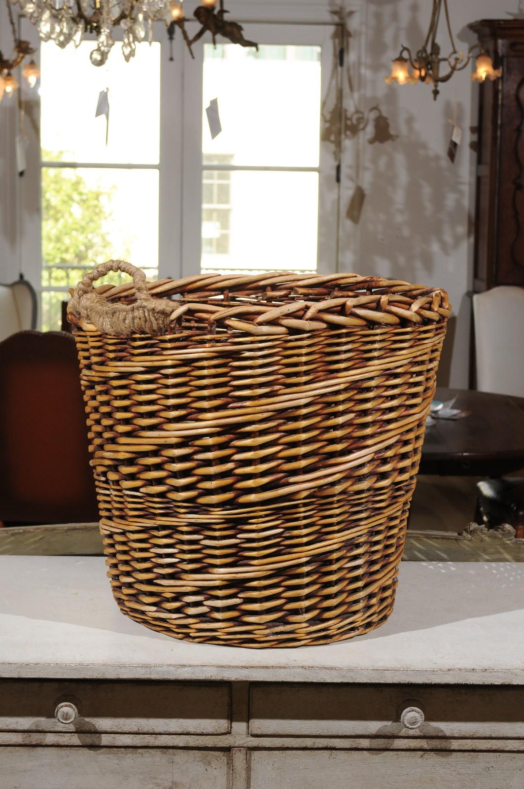 A large French wicker basket from the 20th century, with lateral handle. Rustic yet elegant, this French wicker basket features a tapering body highlighted with diagonal patterns. The woven top presents a single lateral handle allowing the piece to